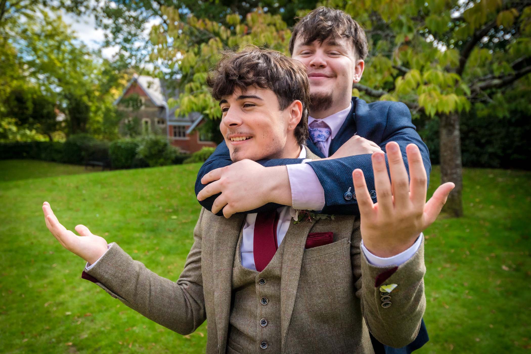 Young man with arm around another's neck at a wedding who has hands raised