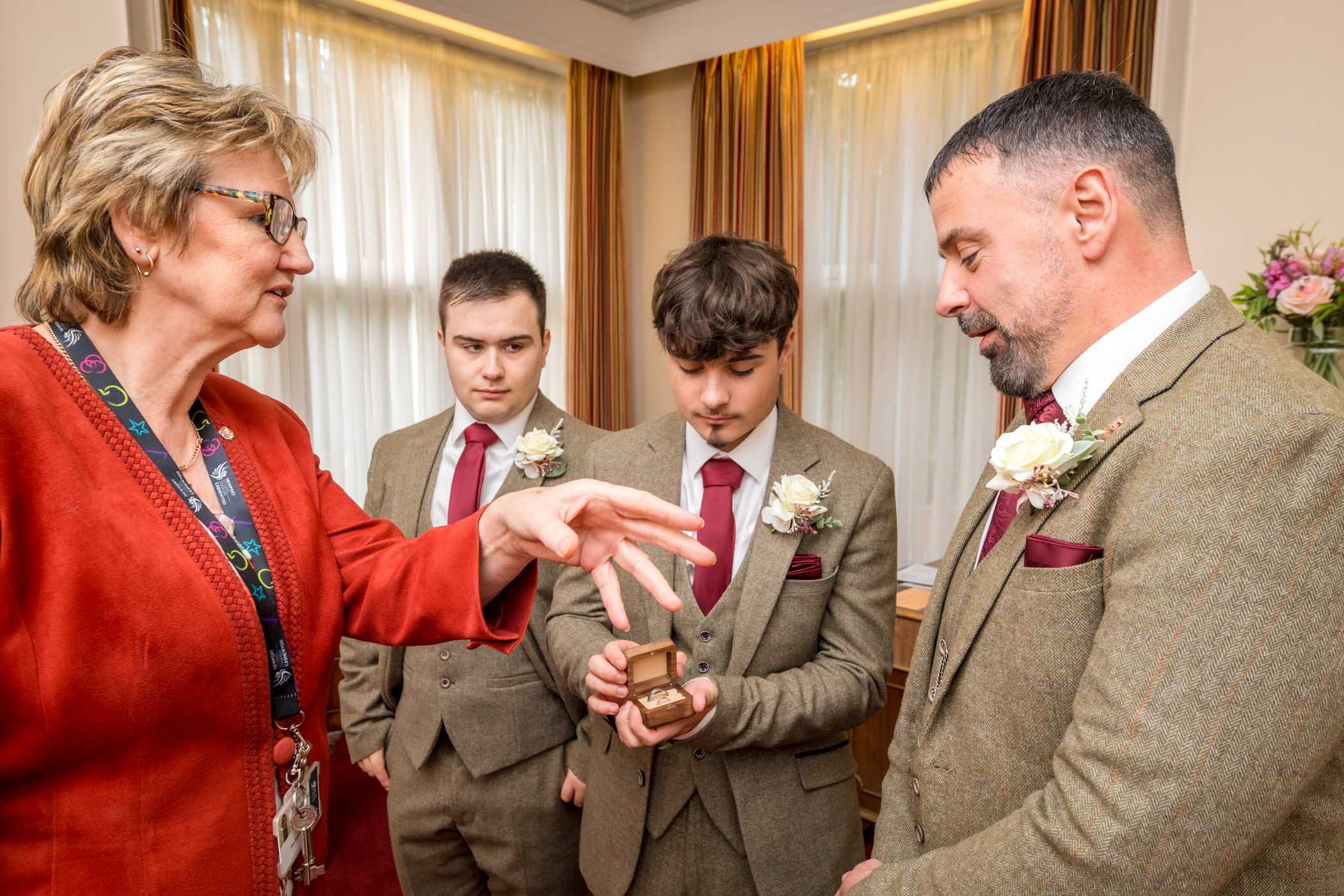 Man with ring whilst groom watches and registrar waves hand