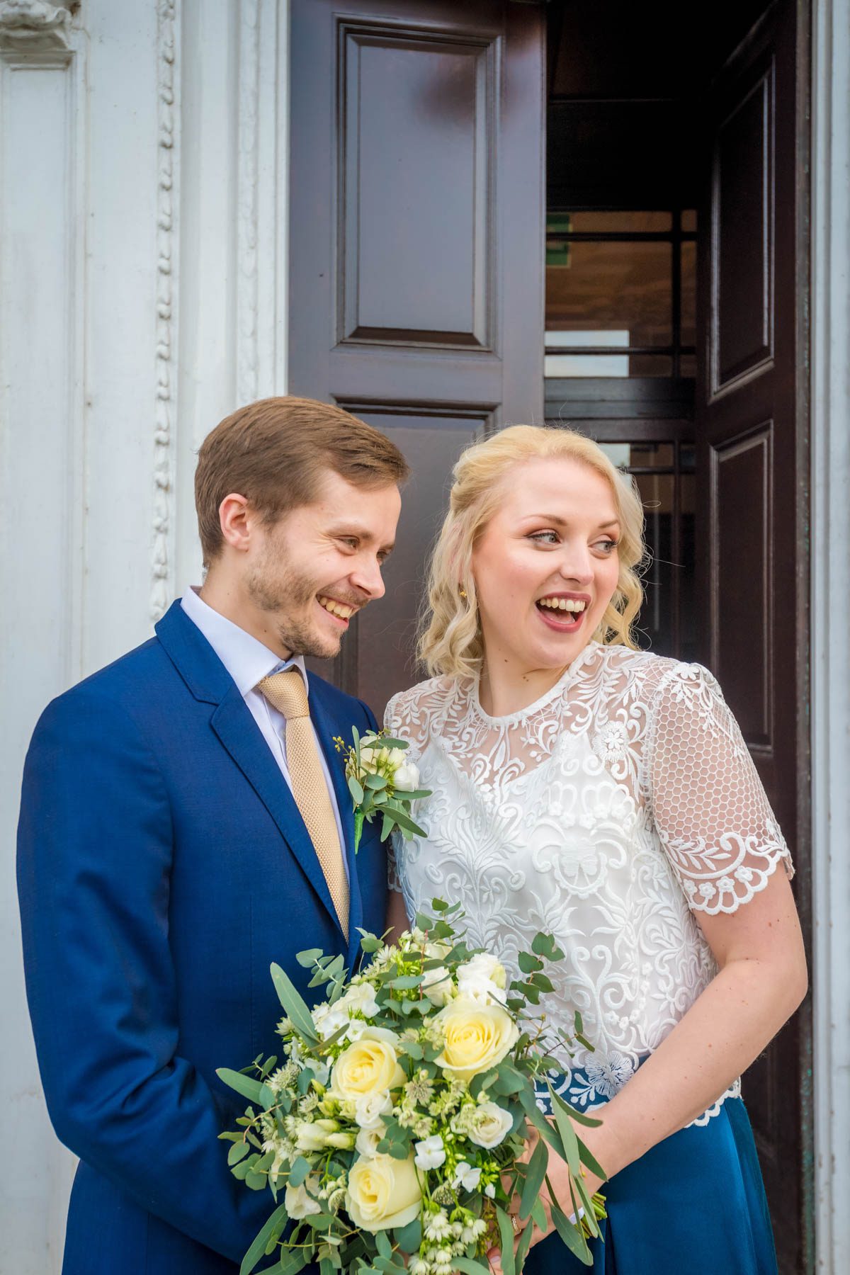 Newlyweds in front of door looking away and laughing.