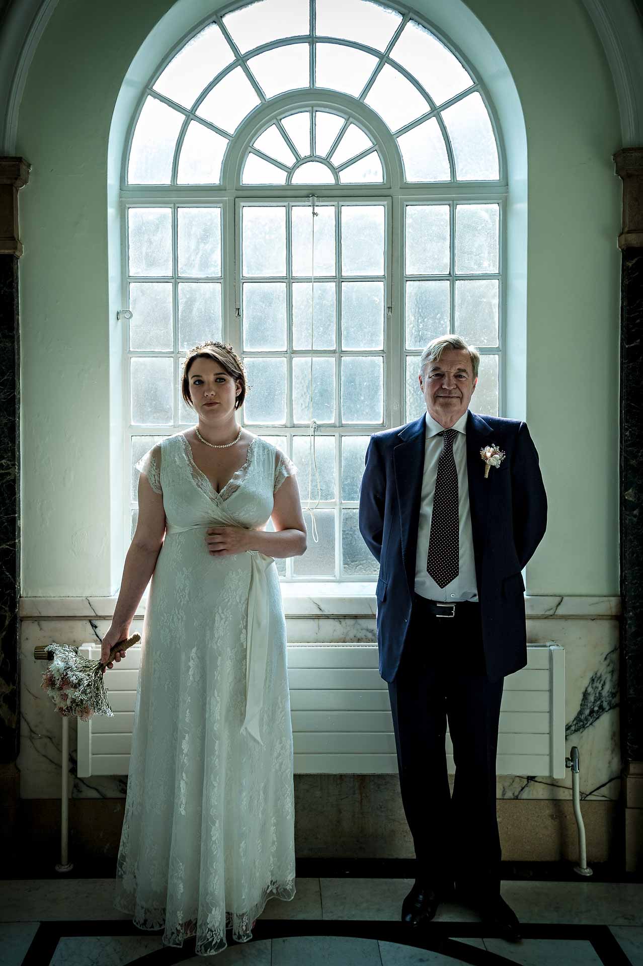 Bride with Father Waiting Infront of Large Arched Windows
