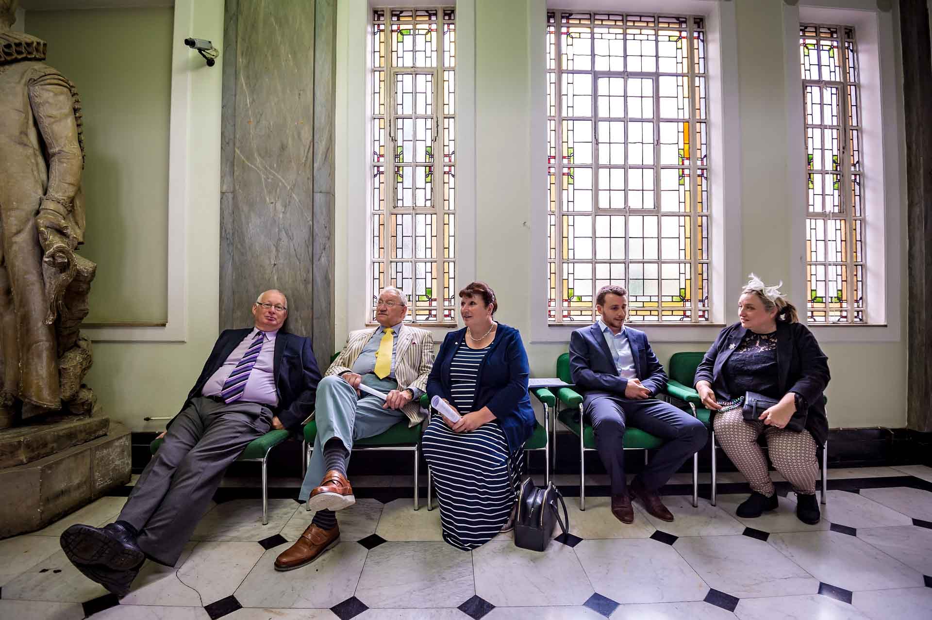 Wedding Guests Waiting in Hall Before Ceremony with Stained Glass Windows in the Background