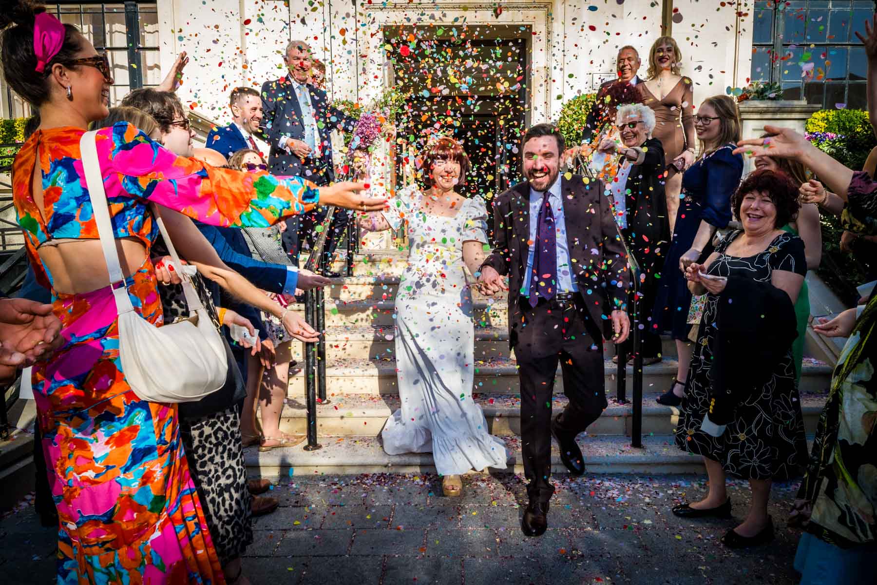 Couple laughing and walking down steps with guests throwing confetti outside Islington Town Hall