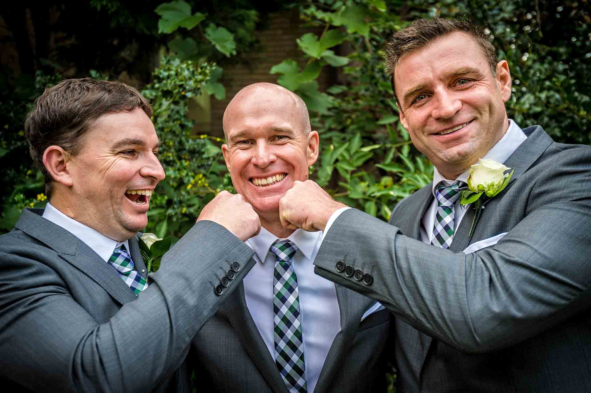 Fun Wedding Portrait of Groom with Friends Pretending to Punch him on the Chin