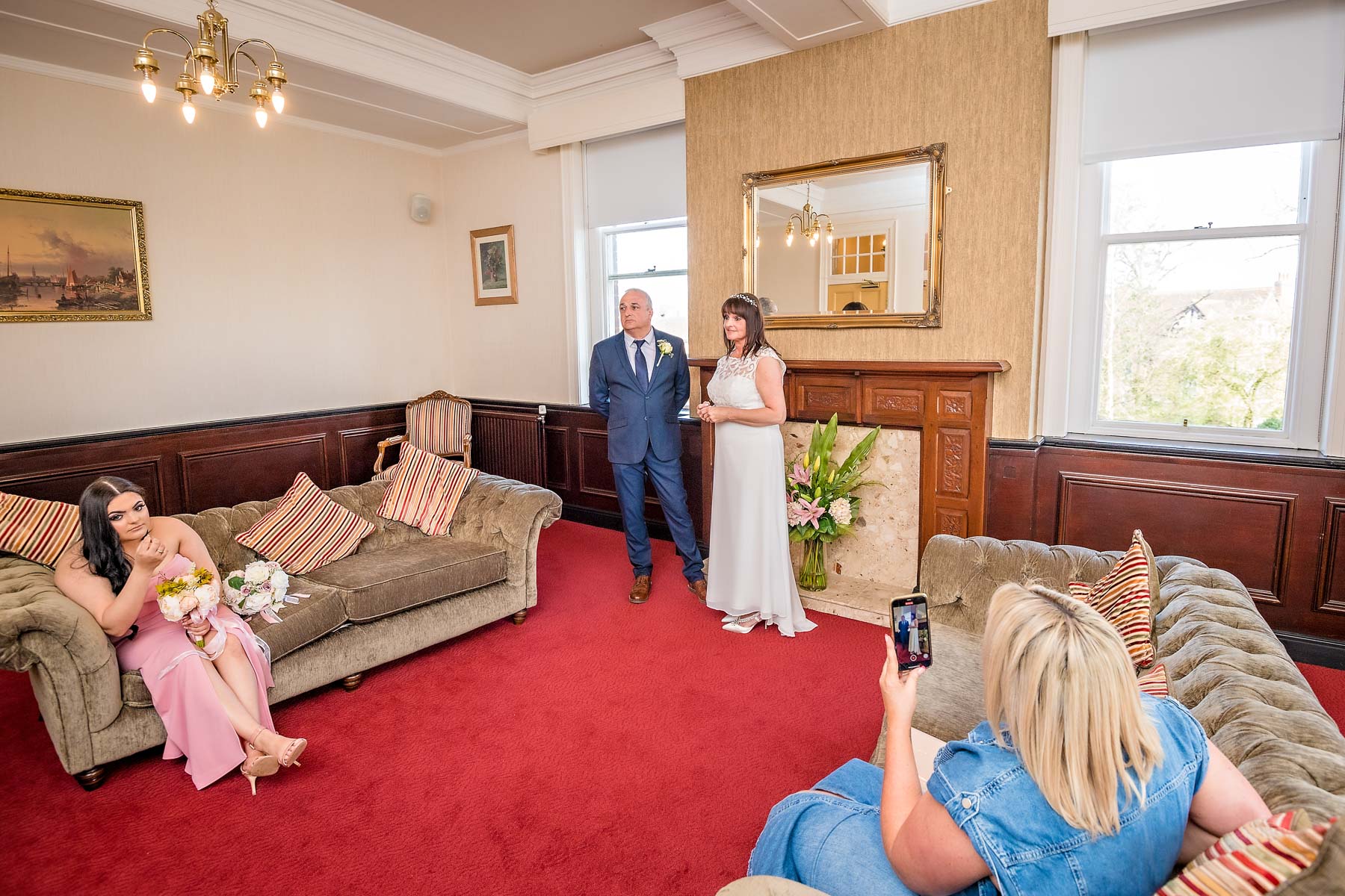 Couple standing in front of fireplace with 2 female guests watching on 2 sofas in the Garden Room at Mansion House, Newport