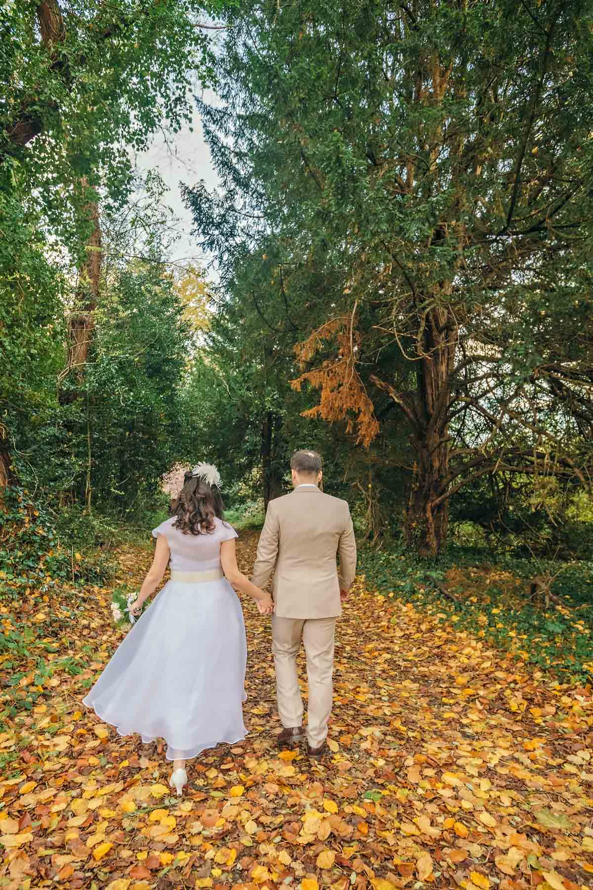 Newlyweds from the back walking hand in hand through Autumn leaves at Bromley Register Office.