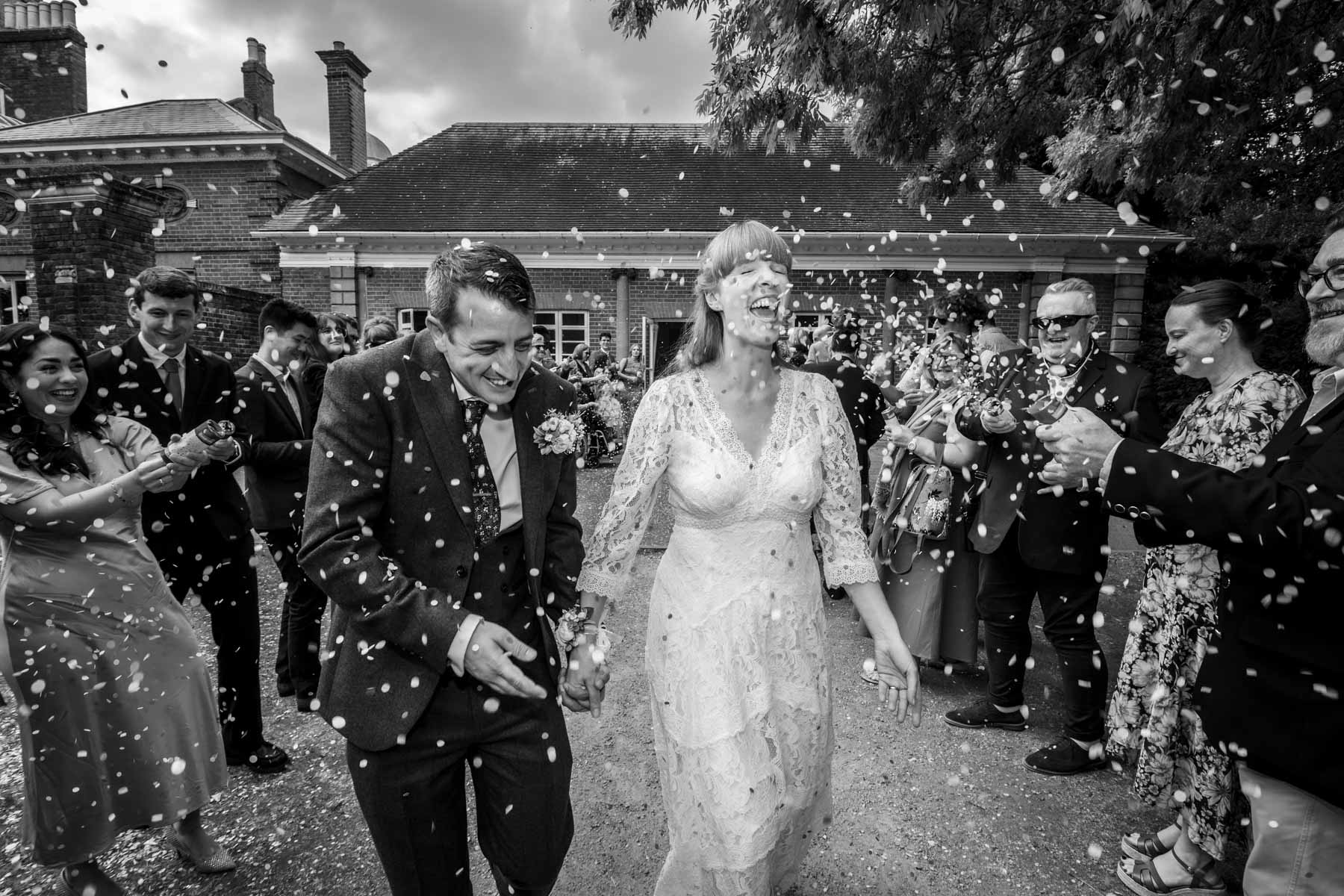 Black and white photo of couple running through a confetti storm in Twickenham