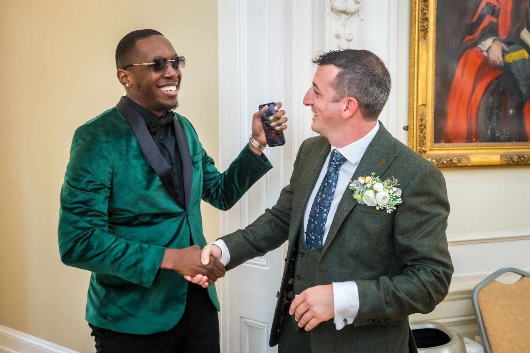 Groom shakes hand with male guest in green at wedding