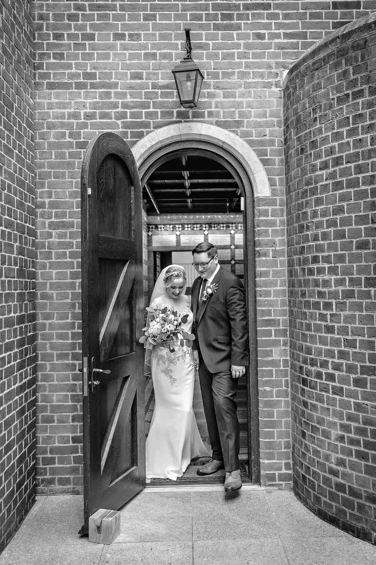 Newly-weds leaving chapel door after wedding in black and white
