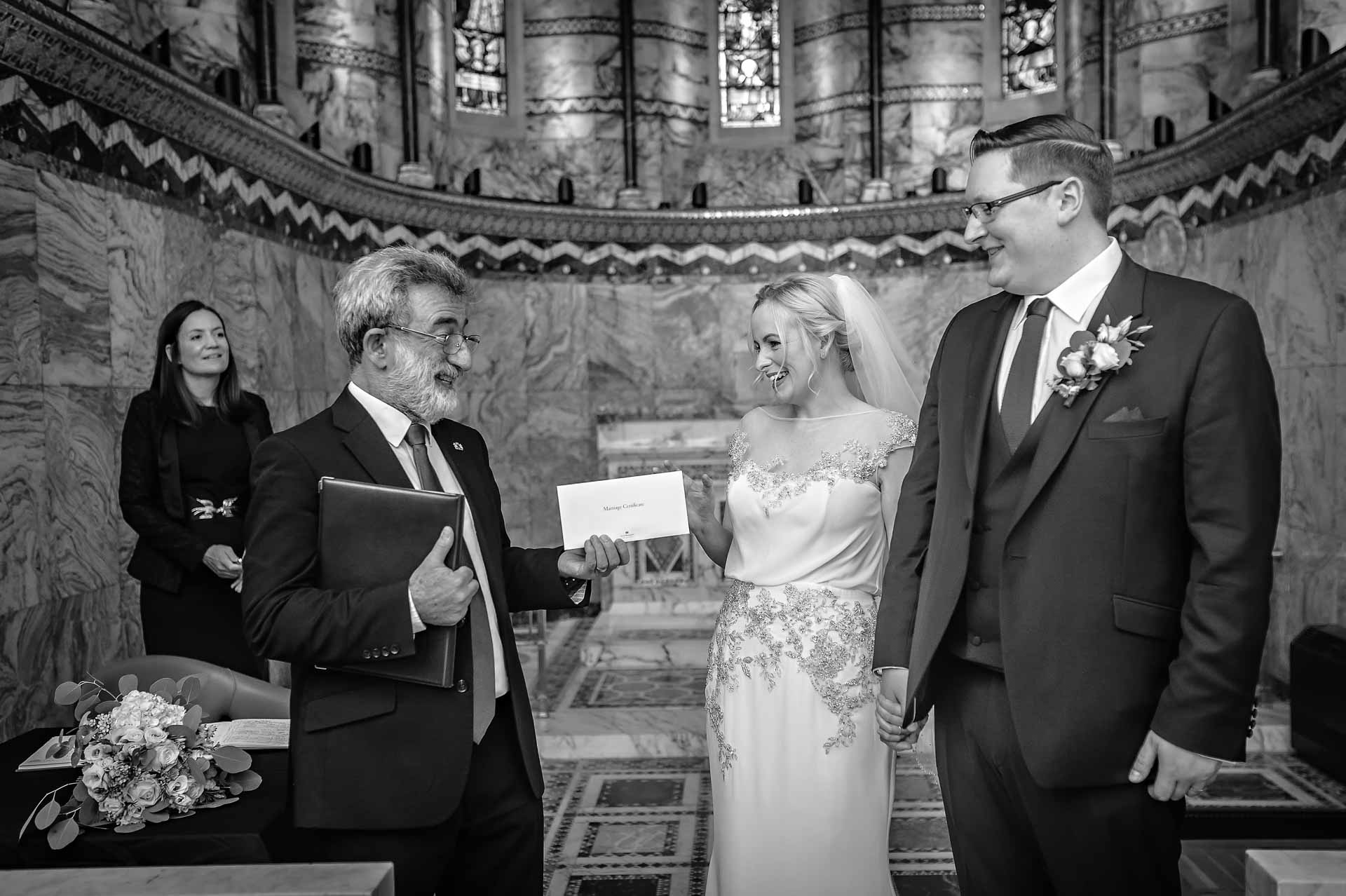 Registrar presenting marriage certificate to newly-wedded couple - black and white photograph