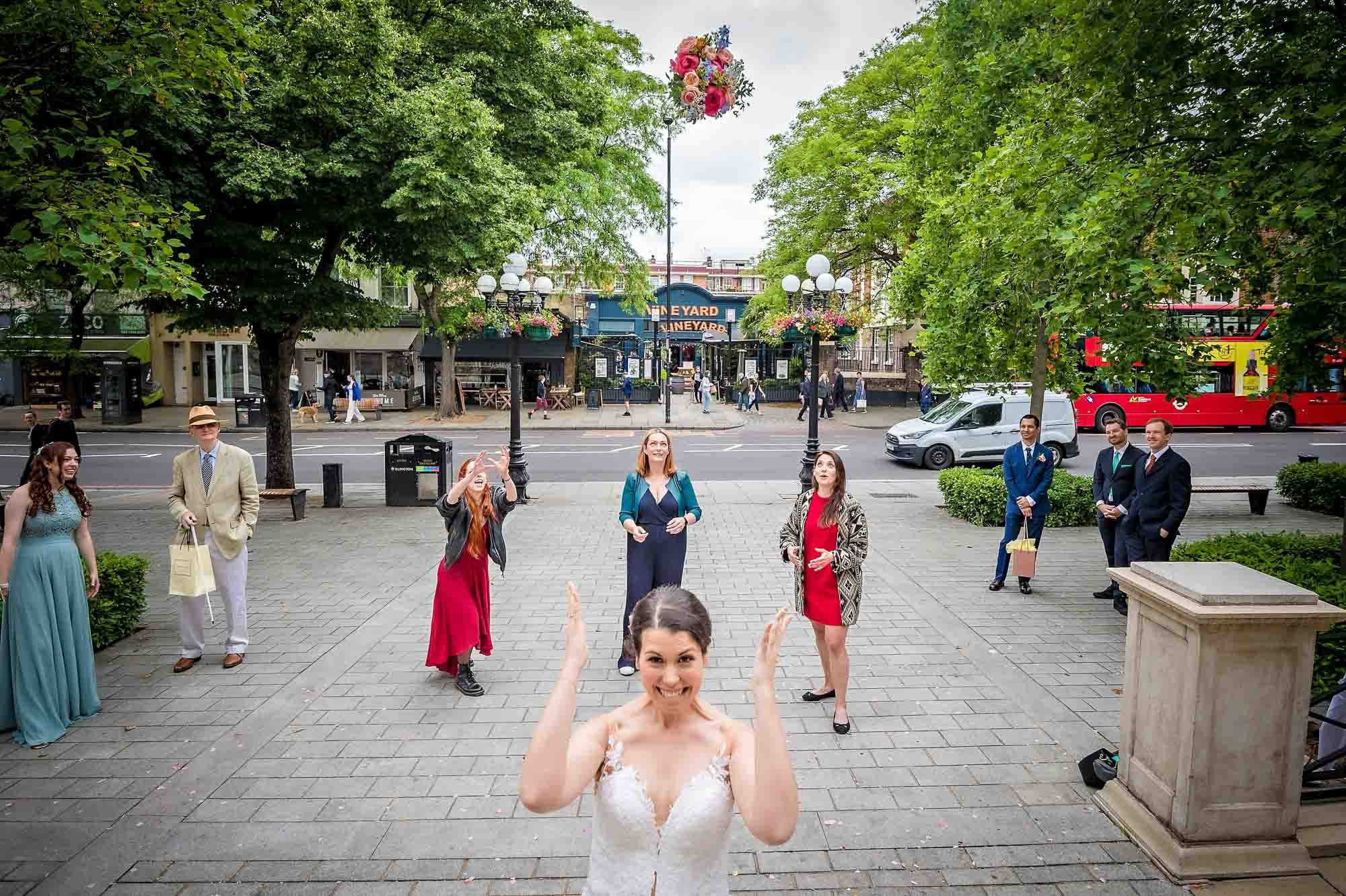 The bride happily tosses her bouquet over her head as three friends try to catch it.