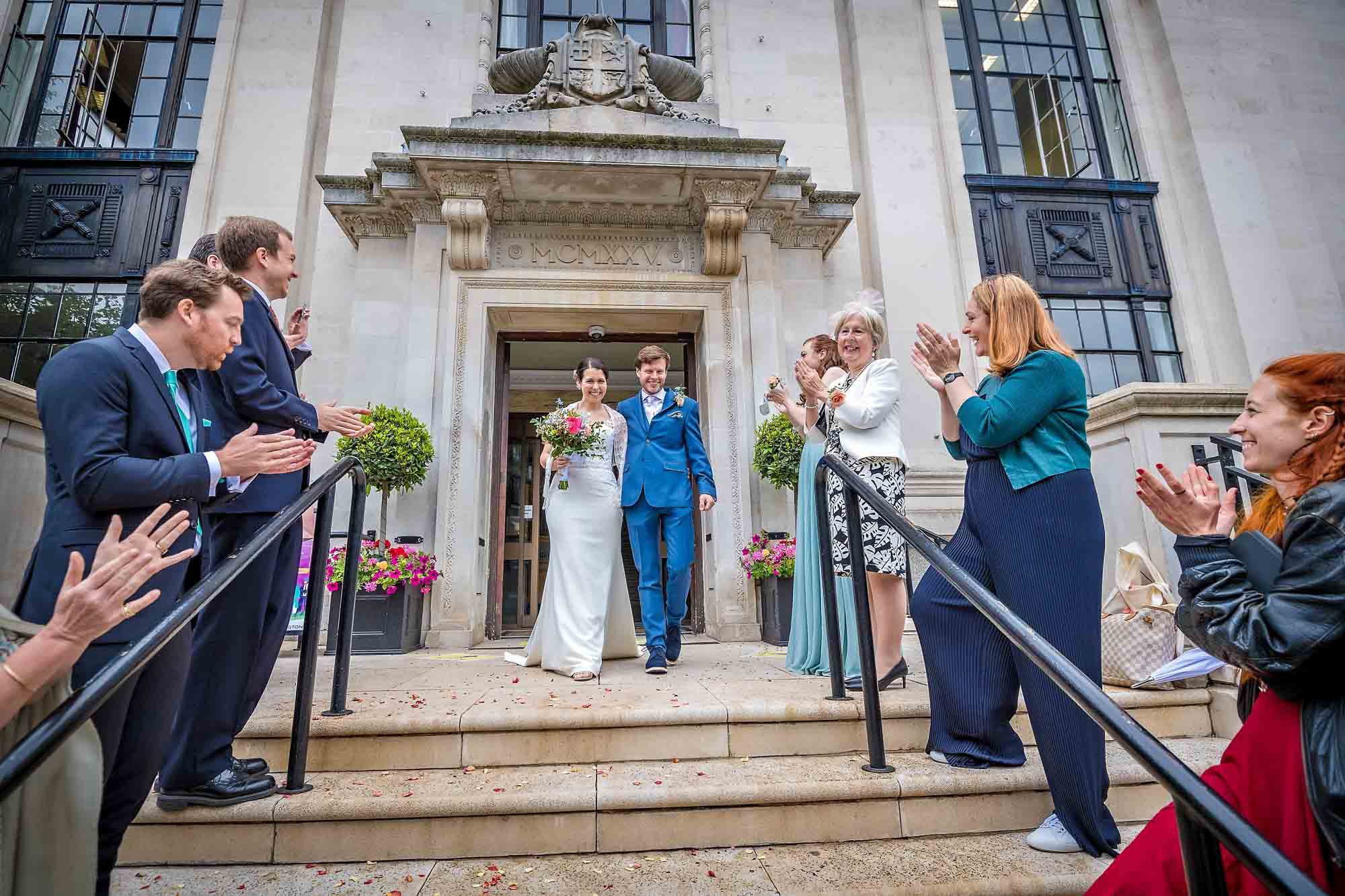 A newly married couple leaving Islington Town Hall with guests clapping them