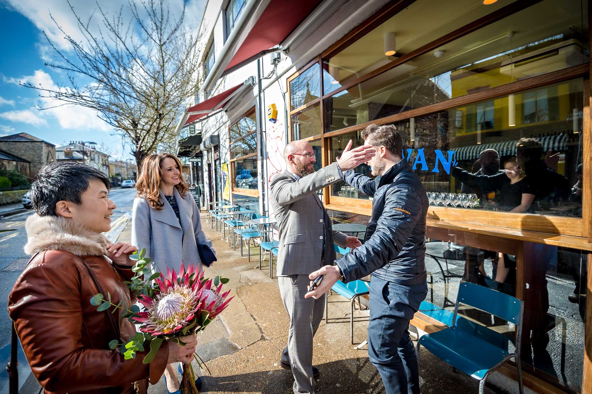 Groom and friend go to hug each other outside Levan Cafe in Peckham