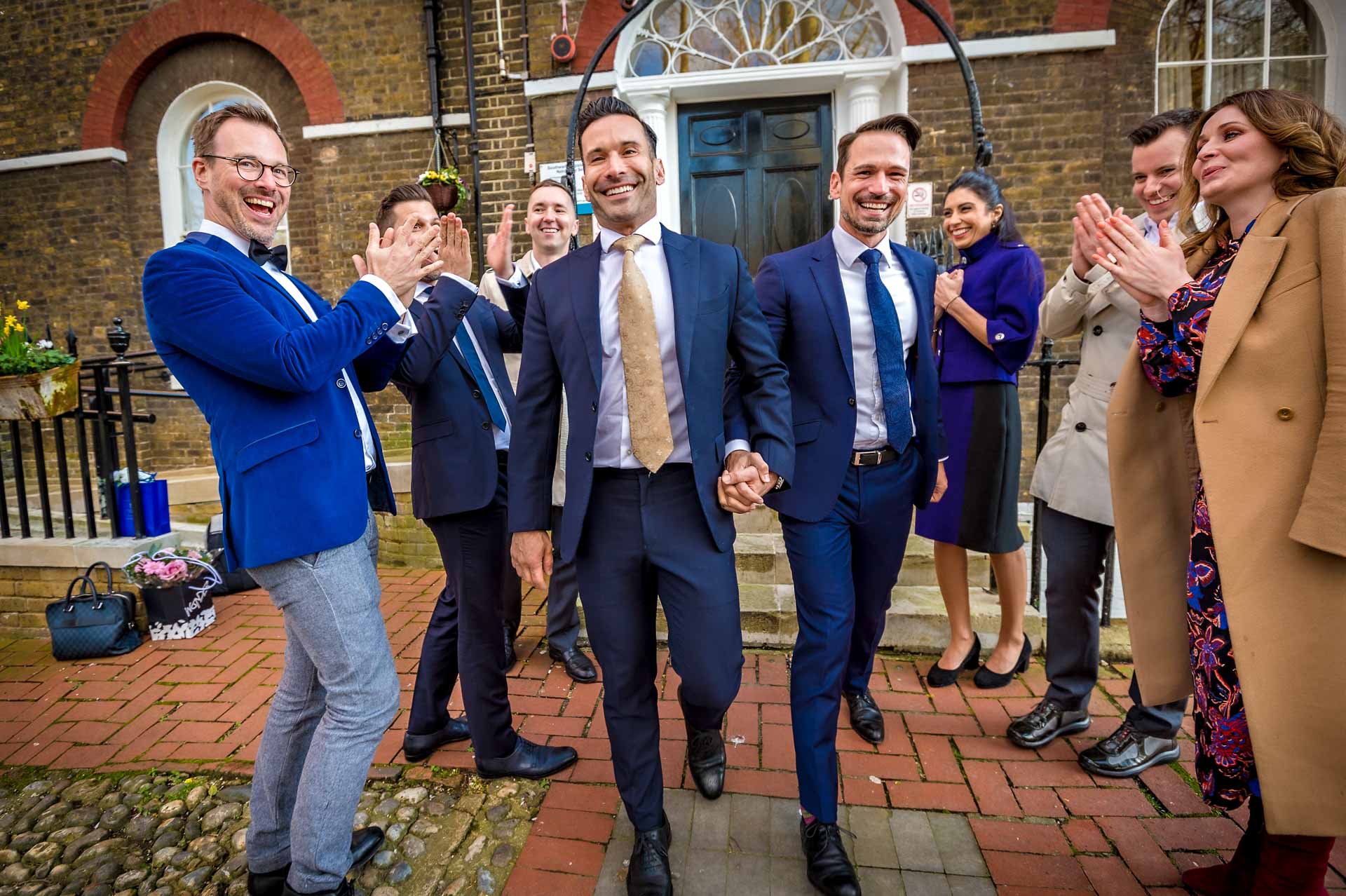 Gay couple leaving Southwark Register Office with guests clapping but no confetti