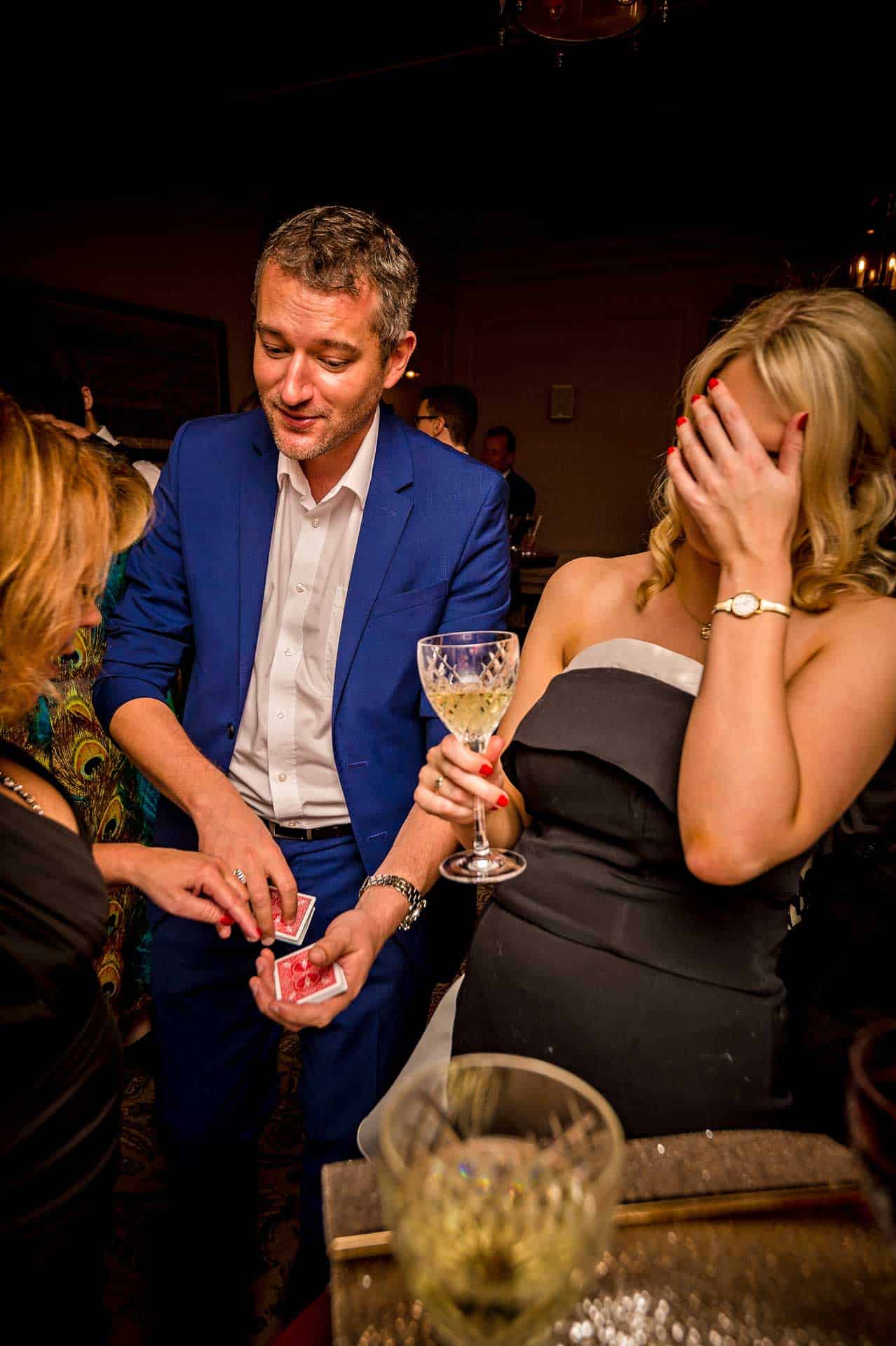 Magician performing card trick and guest covering her face at wedding