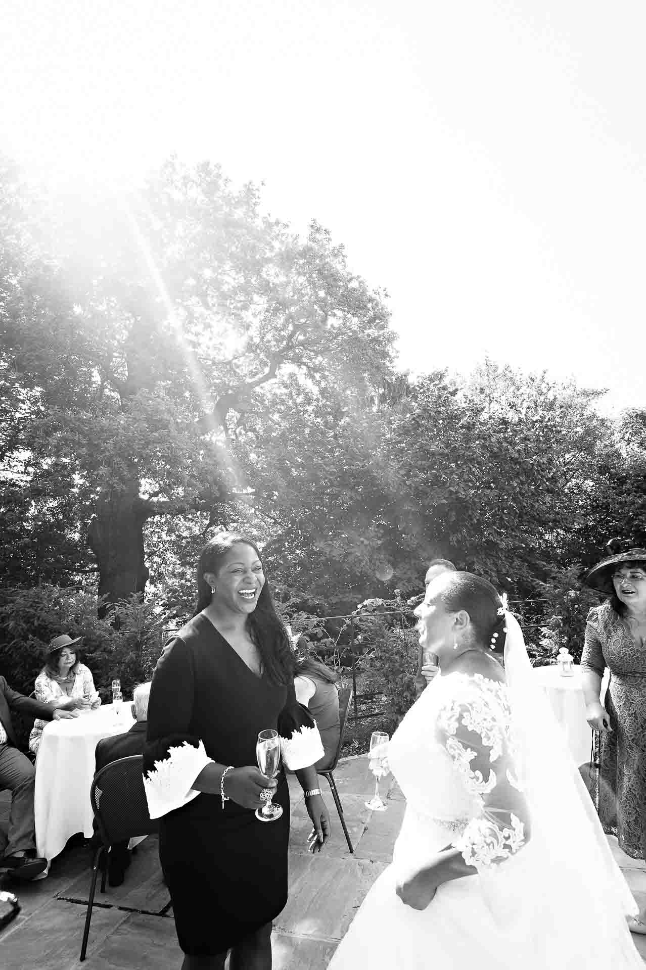 Bride talking with friend in bright sunlight at reception outside Pembroke Lodge