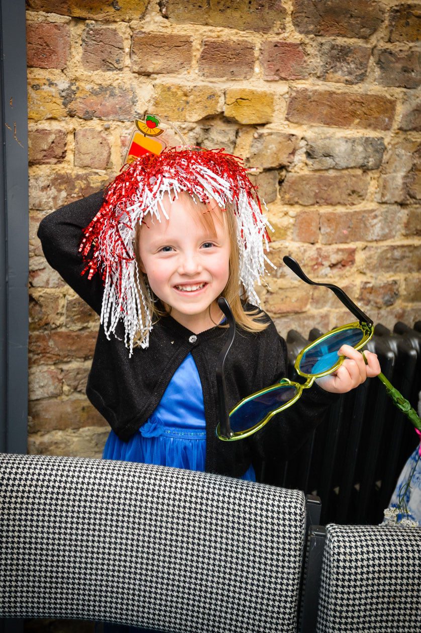 Engaged Couple Looking Down Girl with Party Wig Holding Glasses from Dressing Up Box