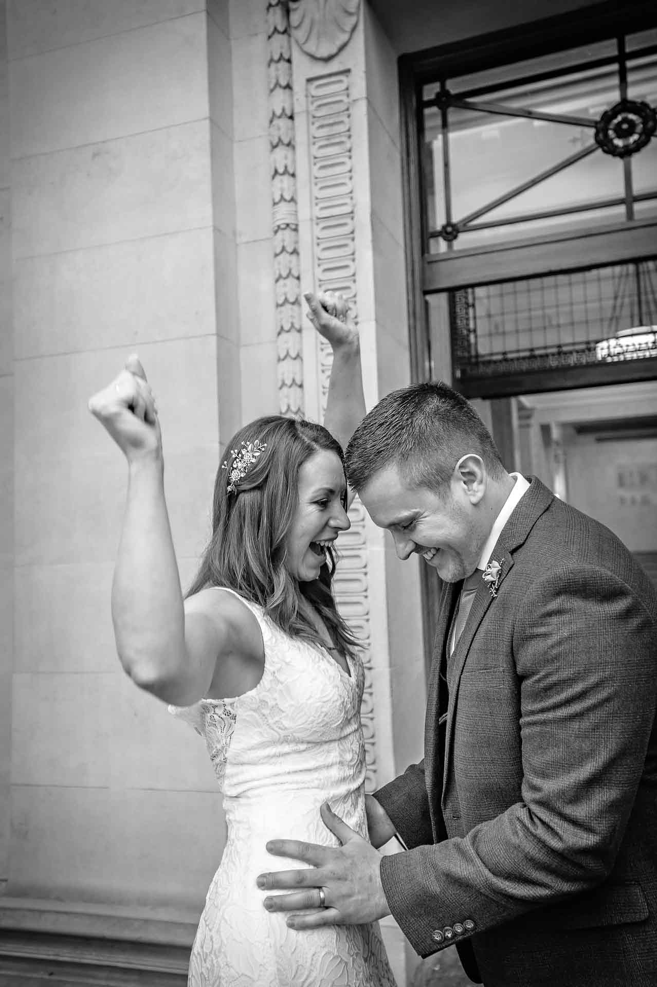 Bride waving arms in the air while groom holds her