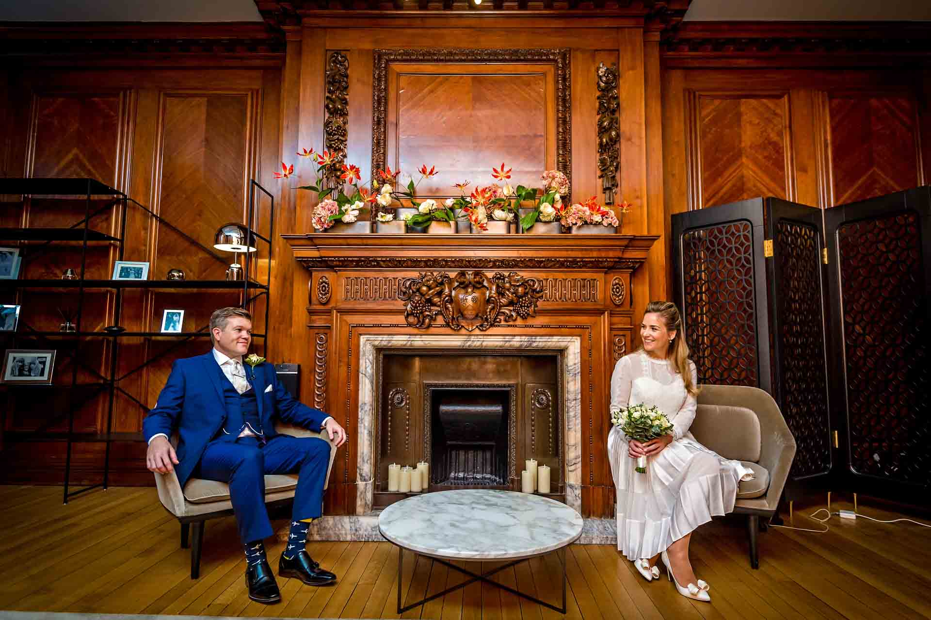 Bride and Groom sitting in front of ornate wooden panelled fireplace