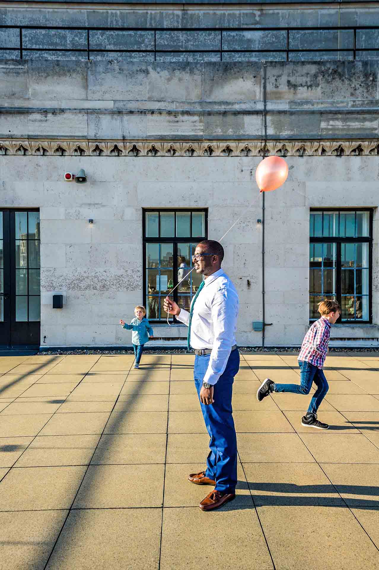 Man standing with balloon whilst children play.