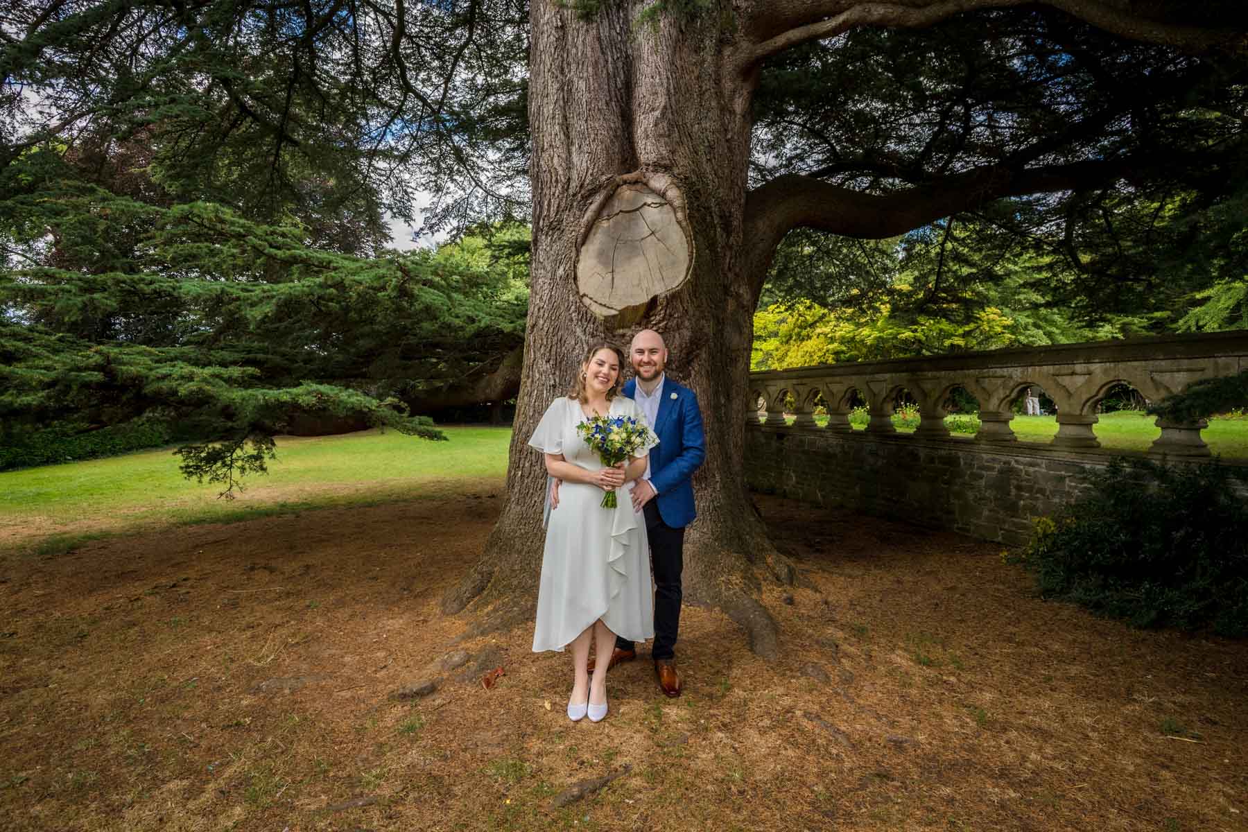 Wide shot of groom holding bride under a cedar tree