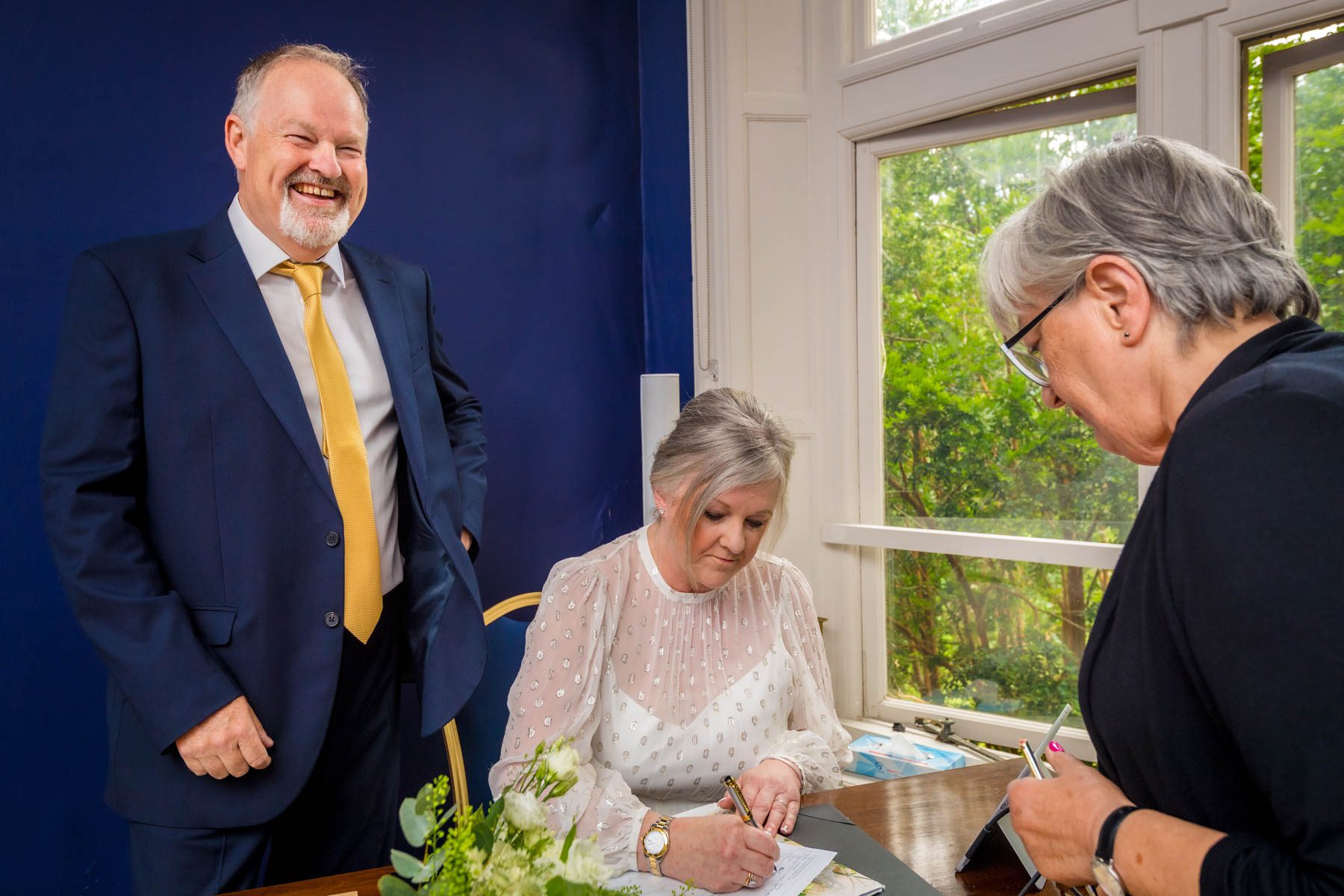 Groom laughing as his bride signs their wedding schedule