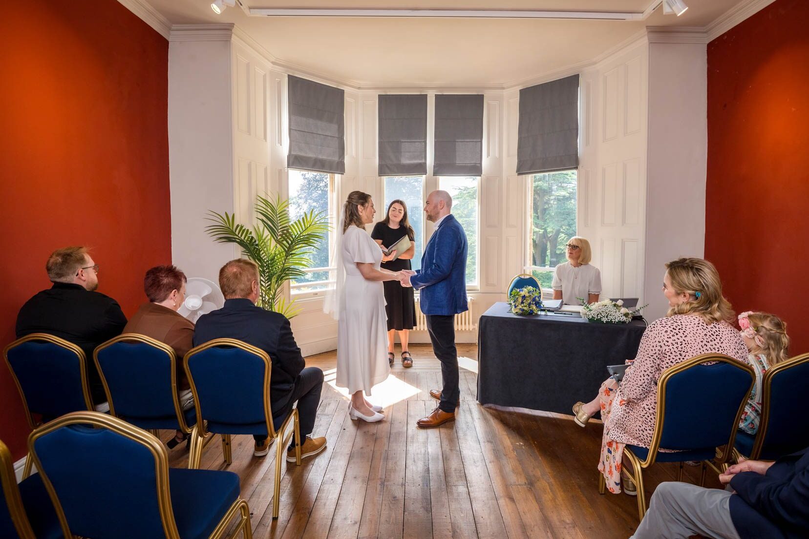 The bride and groom holding hands at the front of the Llandaff suite in Insole Court
