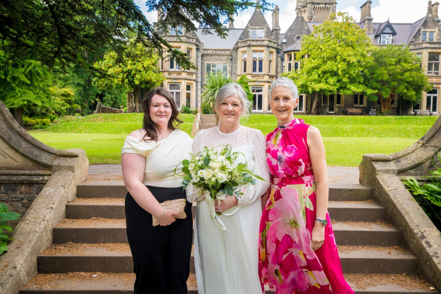 Gay Wedding Couple Walking Down Long Corridor Bride posing with two family members in the gardens of Insole Court