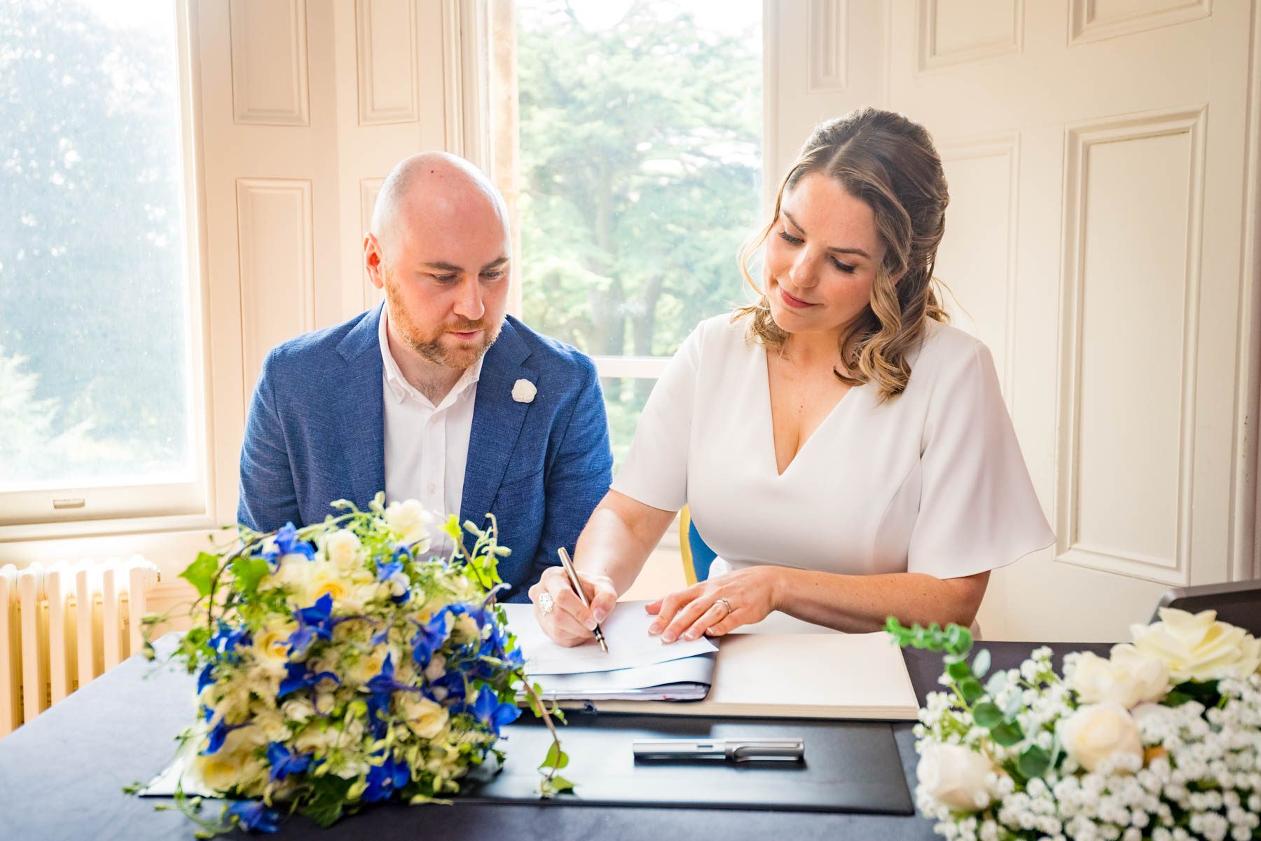 The bride signs the register as the groom looks on at their Insole Court Wedding