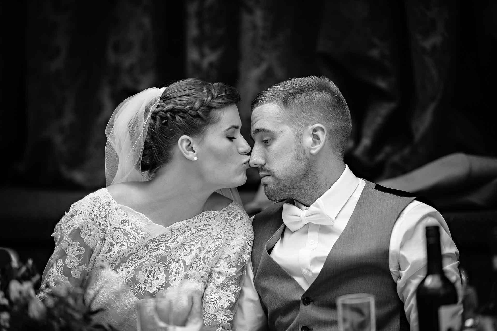 Bride kisses serious groom on the nose at wedding reception