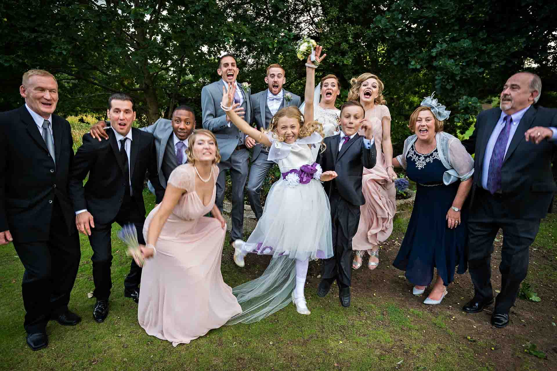 Young bridesmaid leaps into air during the group wedding photos at Hampton Court House