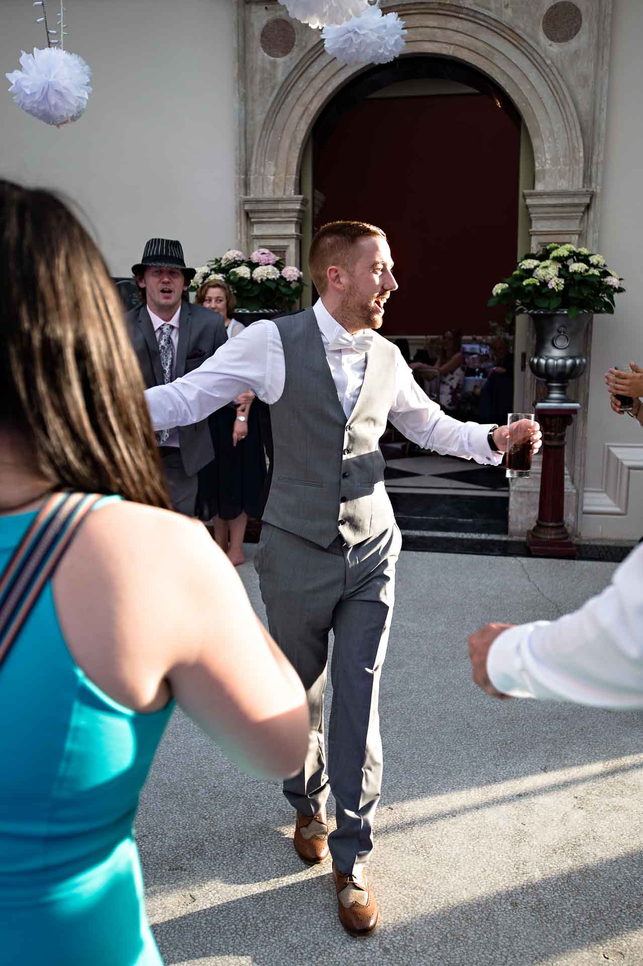 Groom dancing whilst hold drink in the sun at Hampton Court House