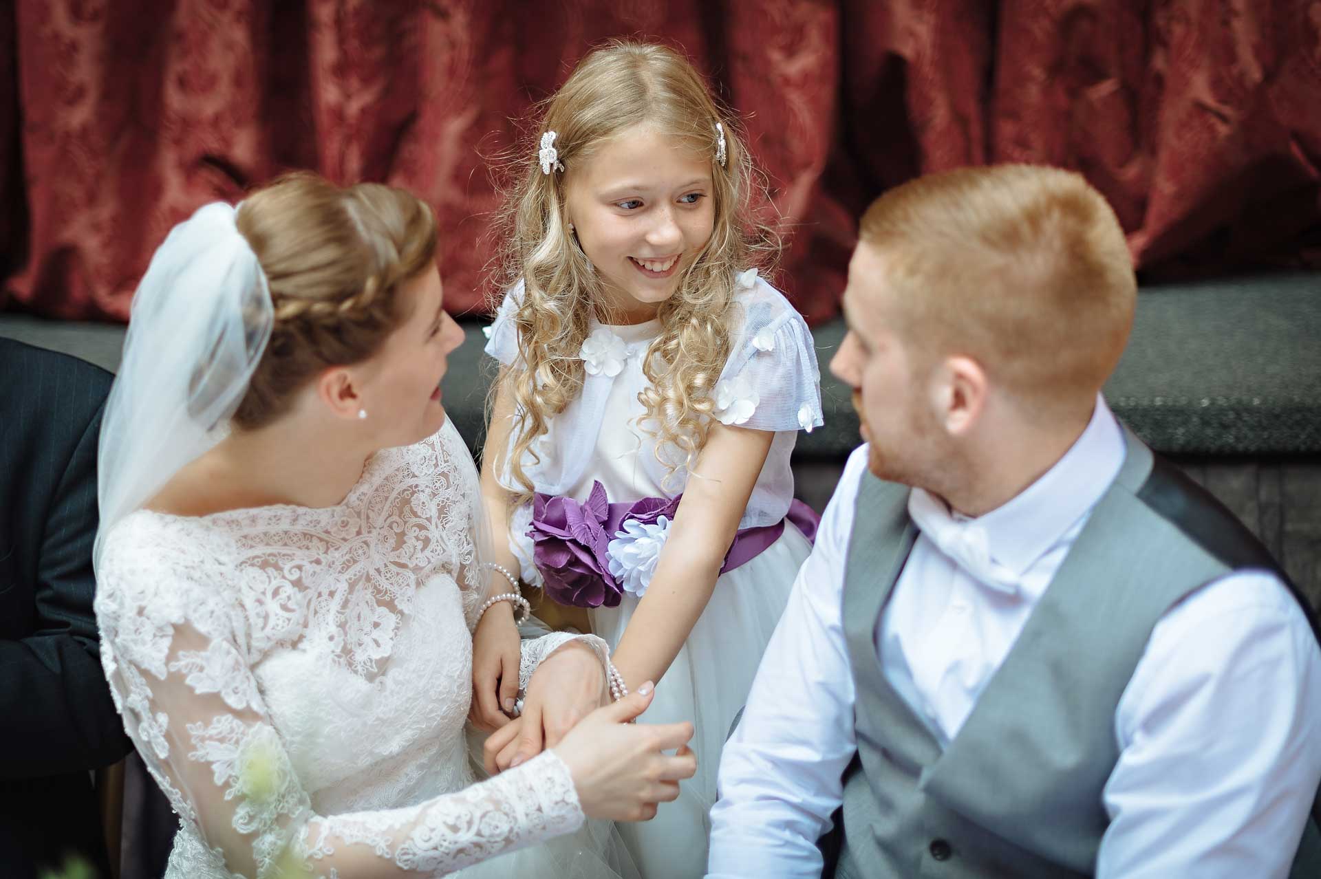 Young bridesmaid smiling between bride and groom in ballroom at Hampton Court House