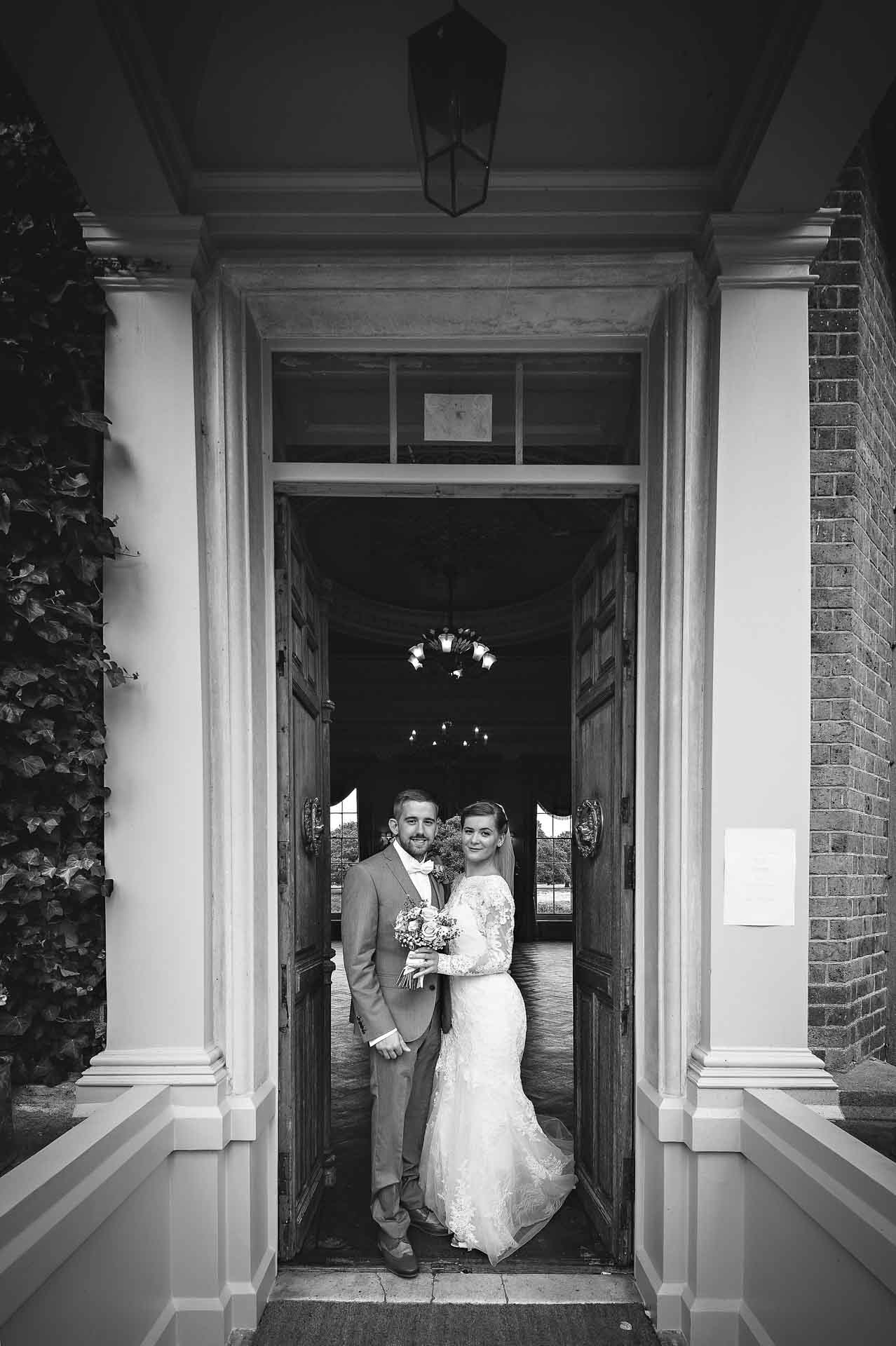 Black and white portrait of the newly-weds in front-door doorway at Hampton Court House