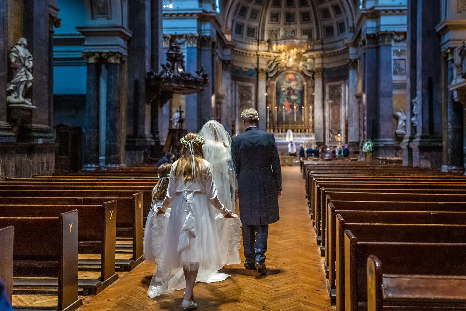 Bridesmaids follow the bride and her father down the aisle of Brompton Oratory