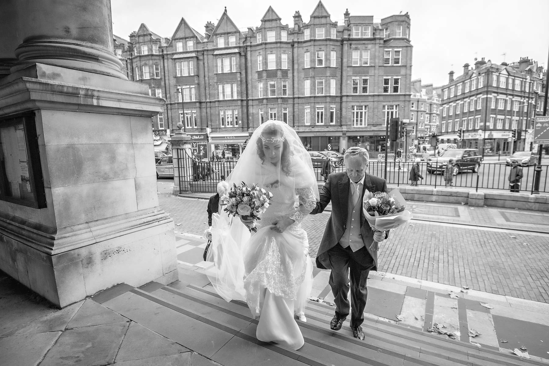 The bride and her father arrive up the steps outside Brompton Oratory for her wedding ceremony