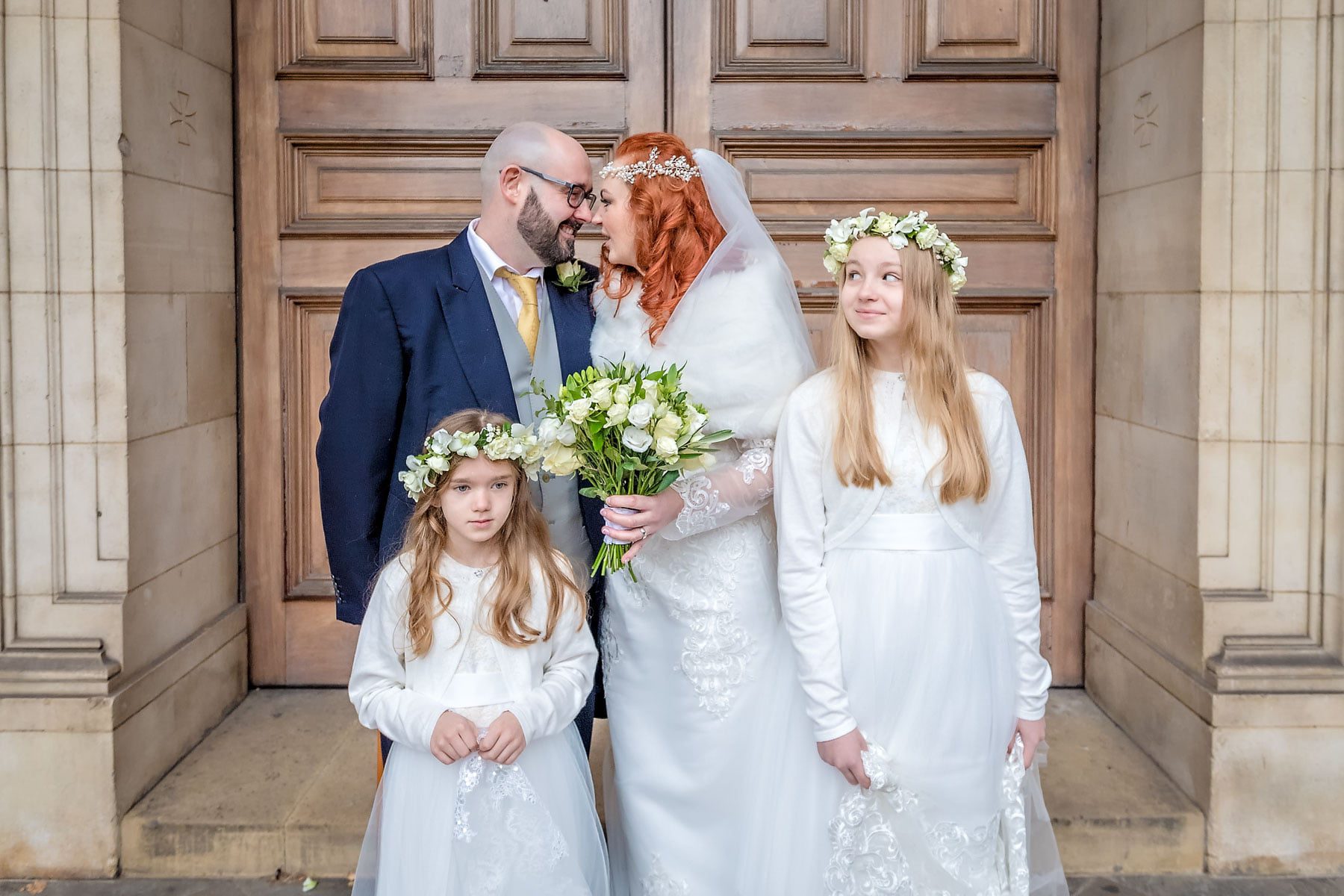 The happy couple looking at each other with bridesmaid daughters at Brompton Oratory