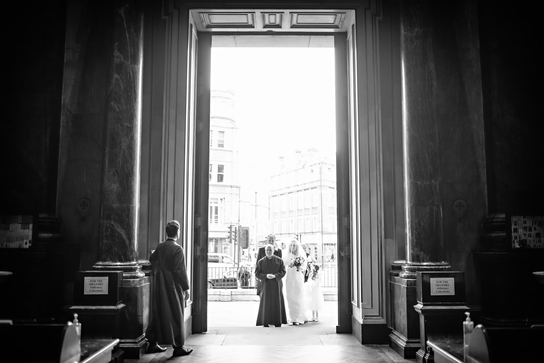 A sacristan opens the huge main doors to reveal the bridal party at a Brompton Oratory wedding