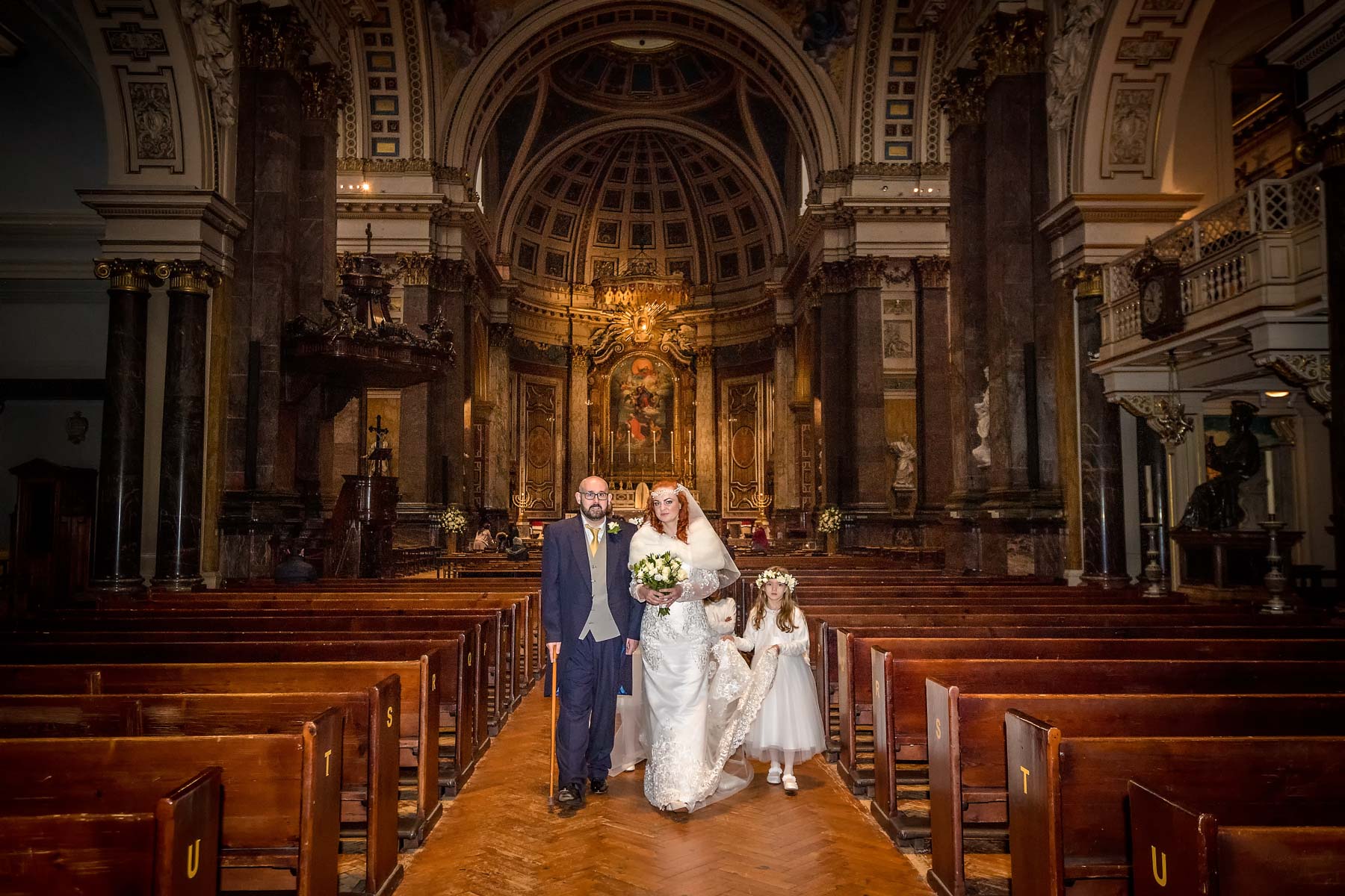The newlyweds and their bridesmaids walk back down the aisle after their Brompton Oratory wedding ceremony