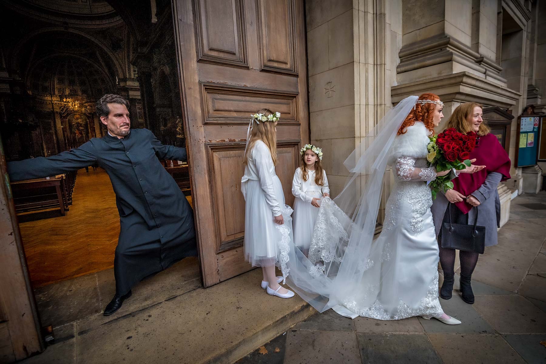 A sacristan closes the main doors at Brompton Oratory whilst the bride chats with a guest after her wedding ceremony