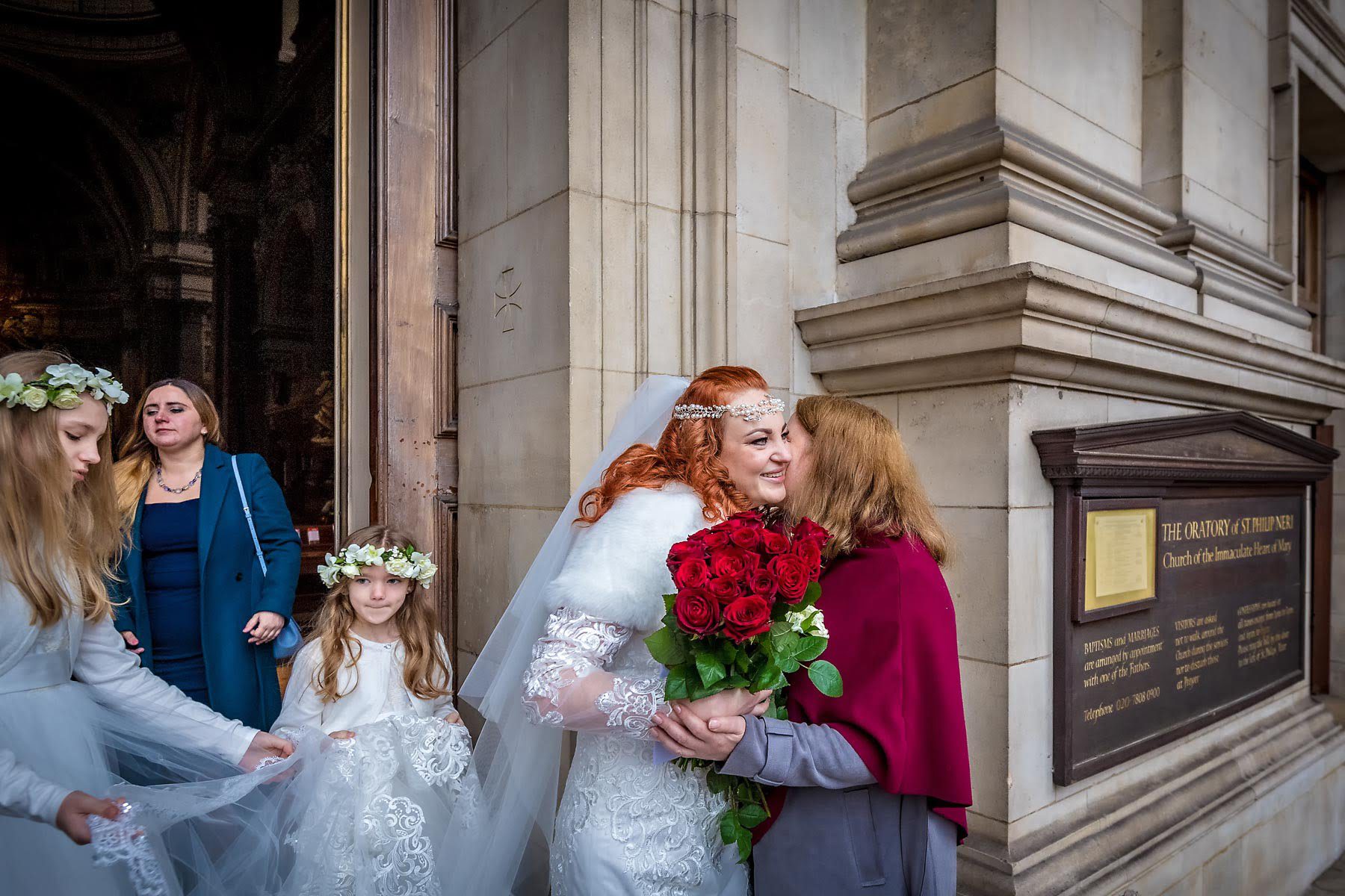 The bride greets a guest with a hug outside her Brompton Oratory wedding