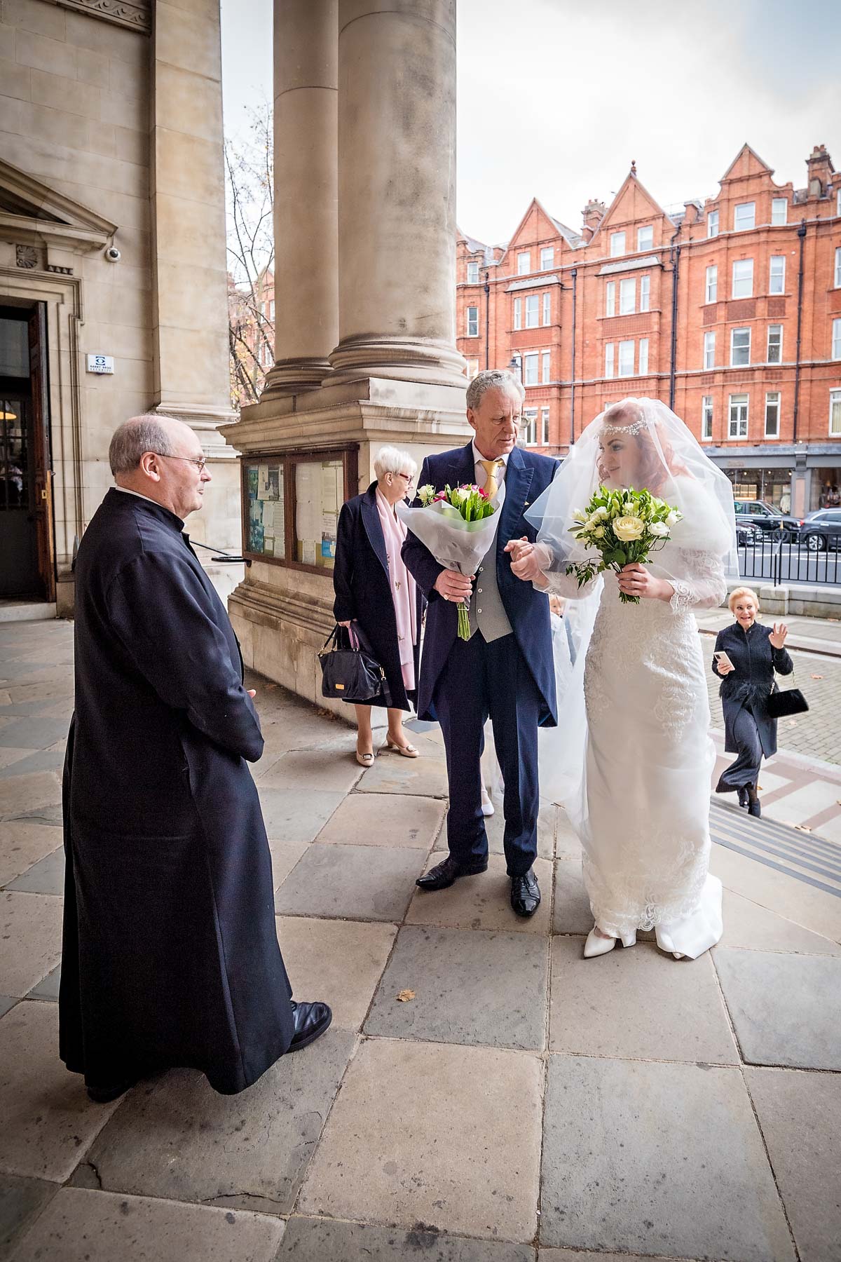 The Head Sacristan greets the bride and her father on the steps of Brompton Oratory
