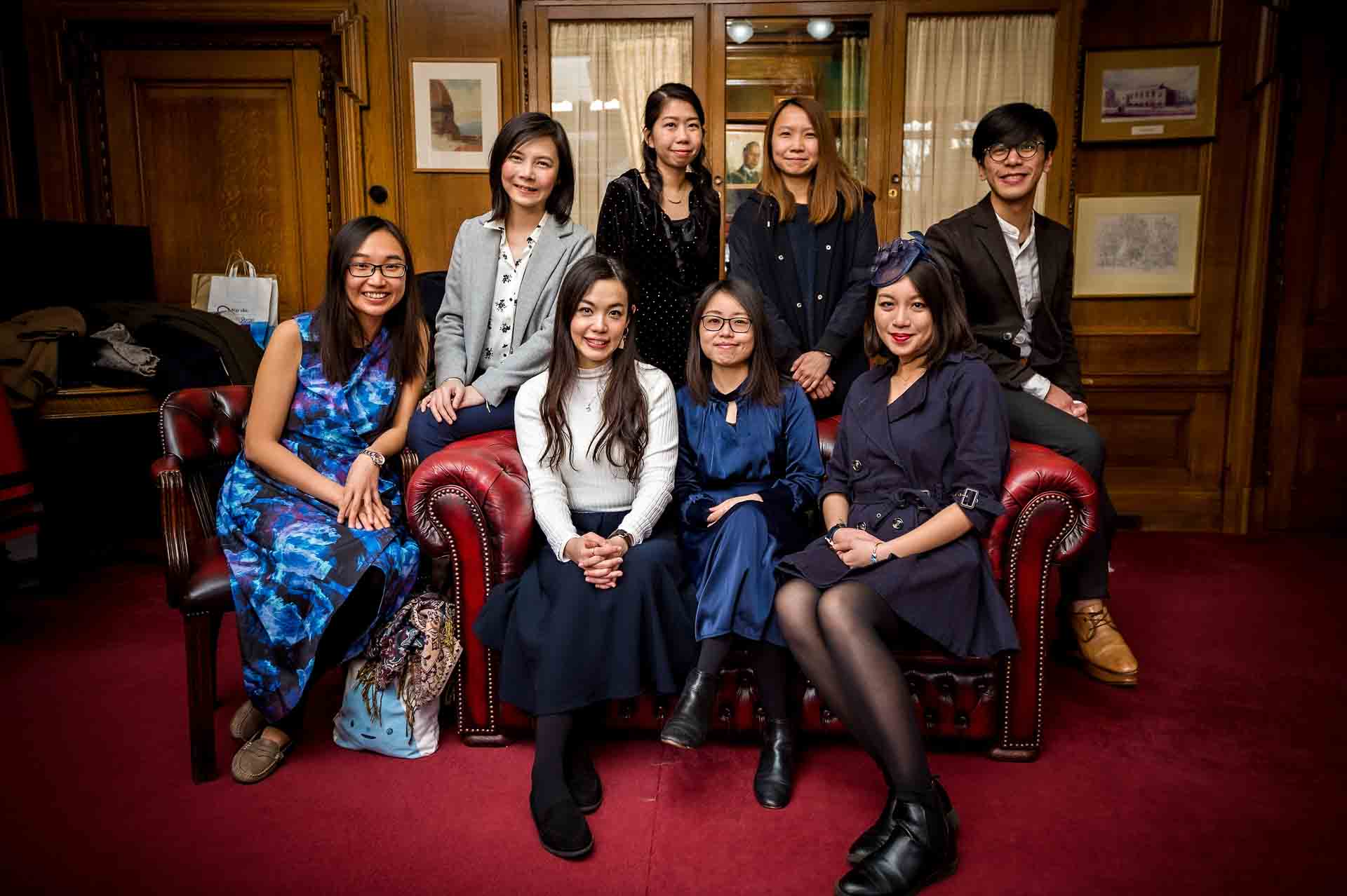 8 guests pose on Chesterfield sofa before wedding in Mayor's Parlour at Islington Town Hall