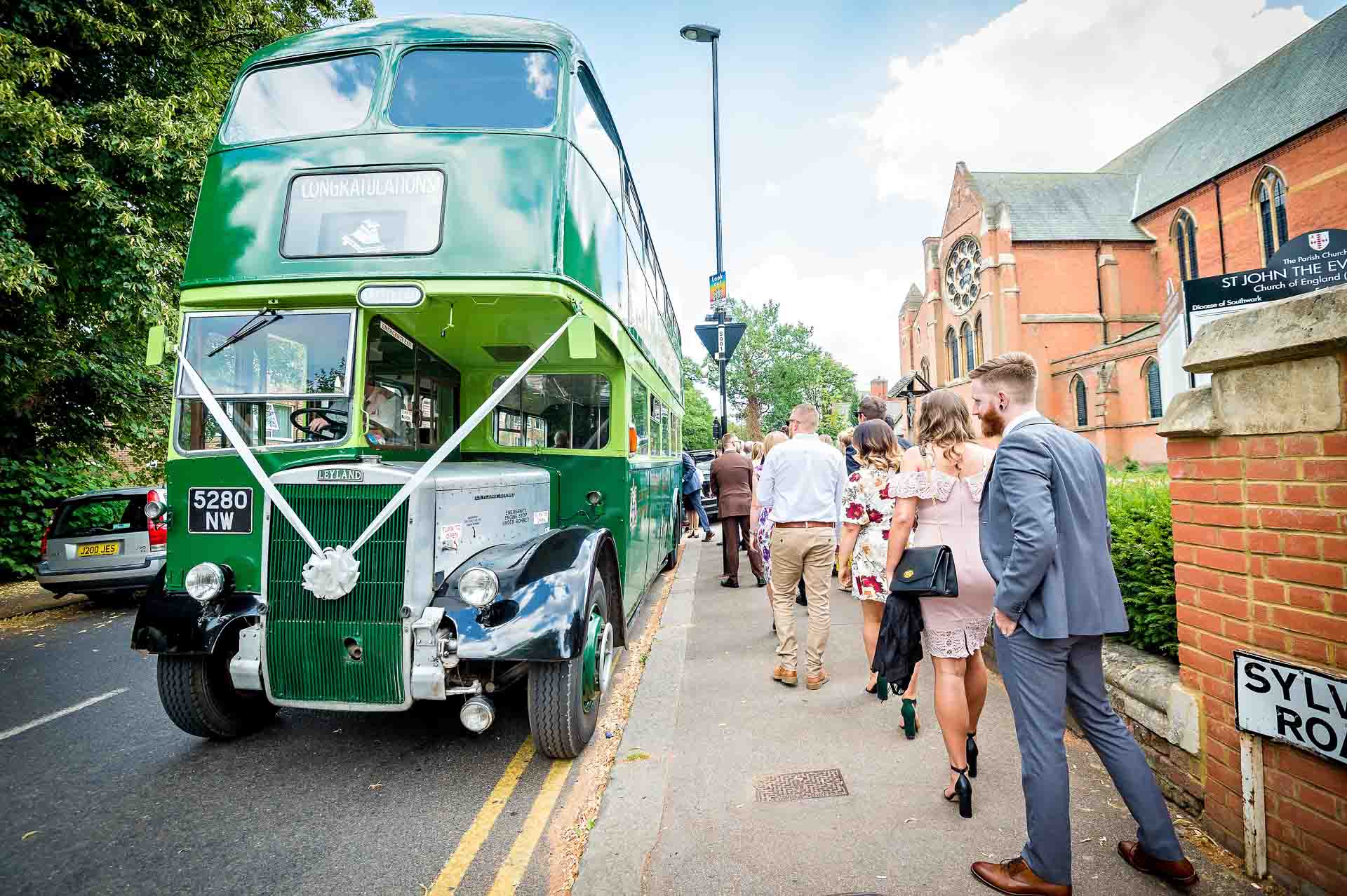 Wedding guests boarding green Routemaster bus outside church