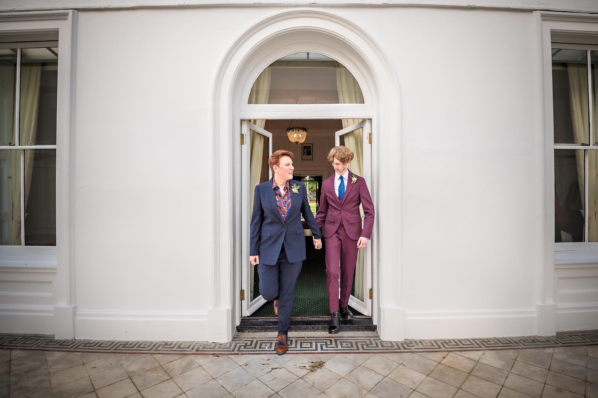 LGBTQ couple leaving wedding ceremony via Functio Room door to garden at the Old Palace in Bromley