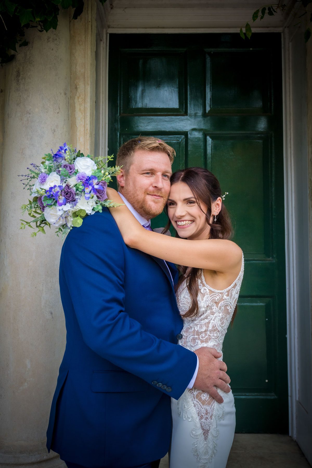 Wedding portrait of bride with her arms around the groom's neck - green door in background