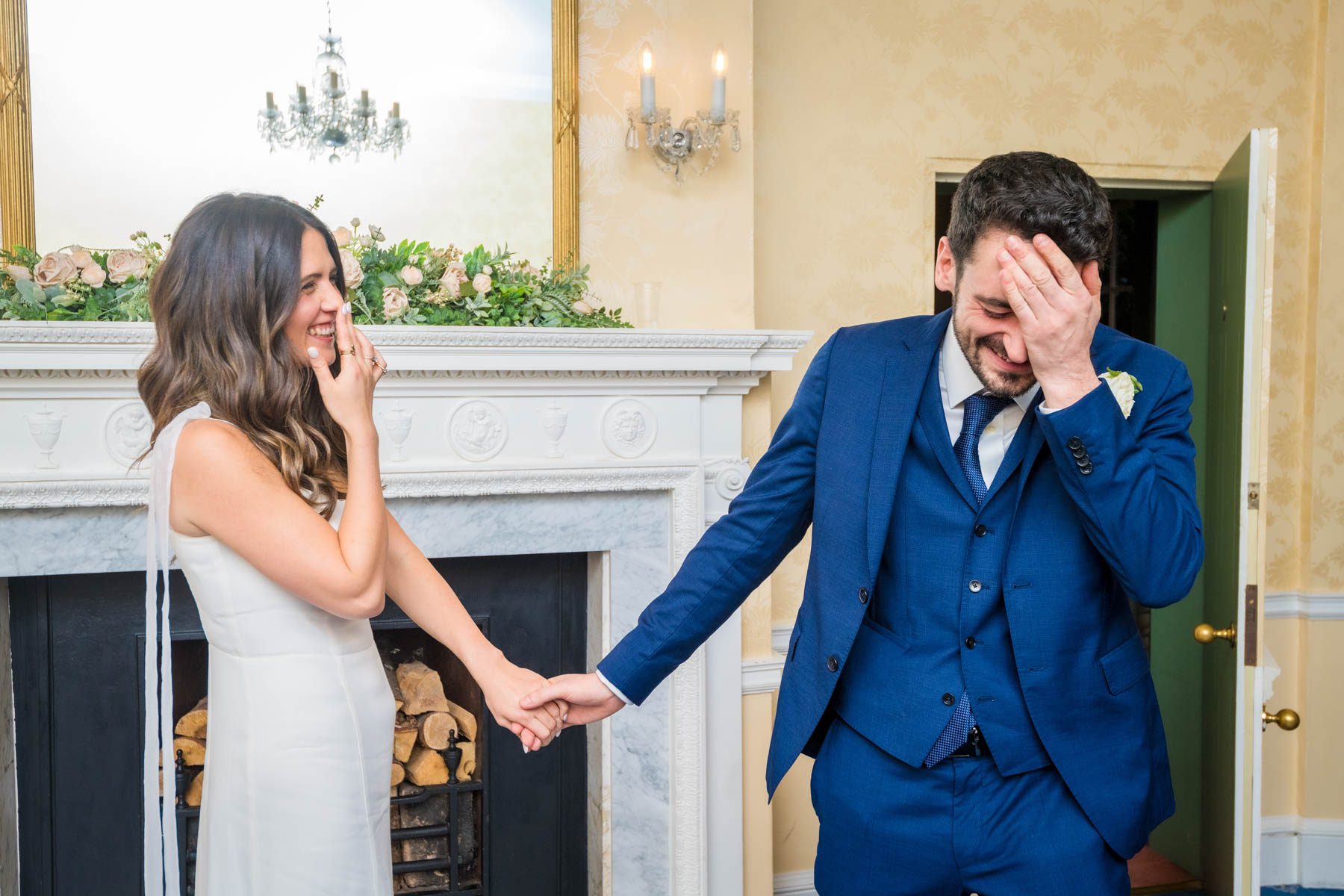 Groom with hand over face whilst bride laughs at wedding in Morden Park House