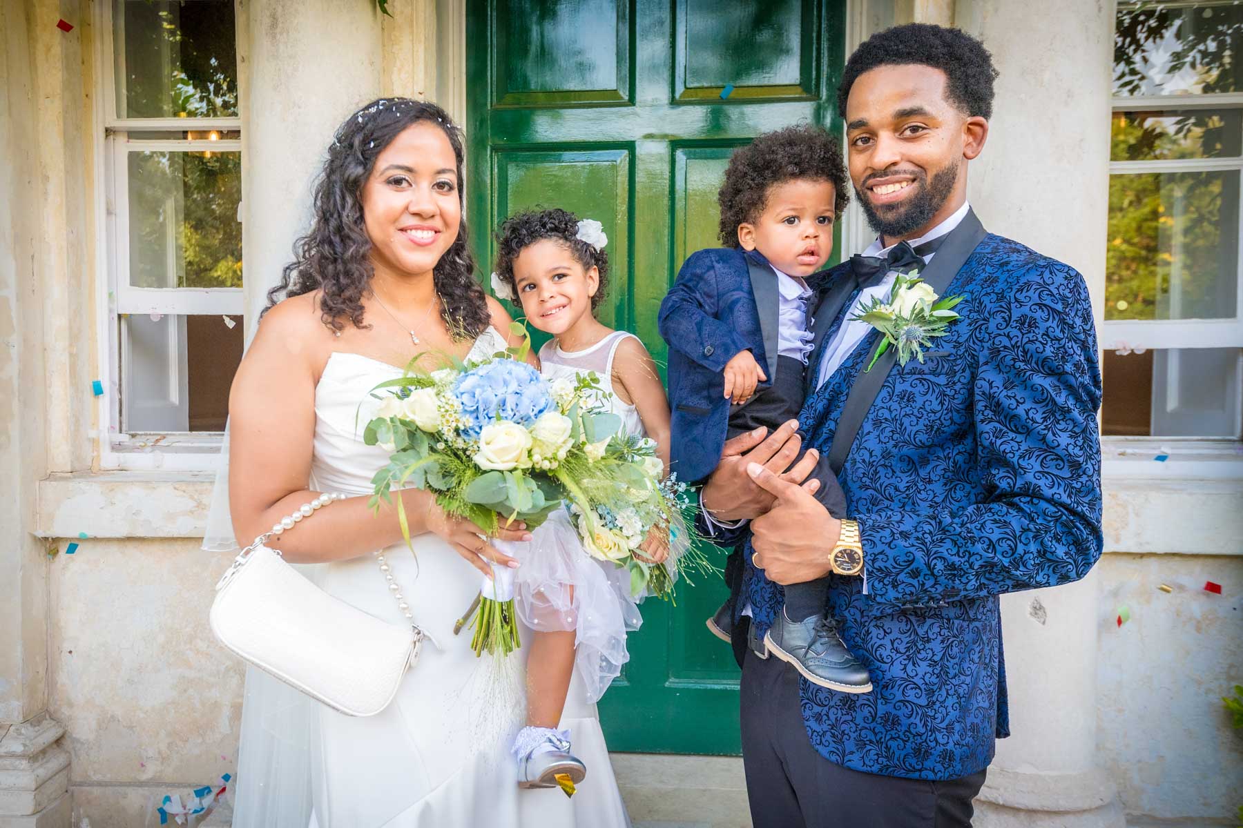 Bride and groom holding their children outside the front door at Merton Register Office