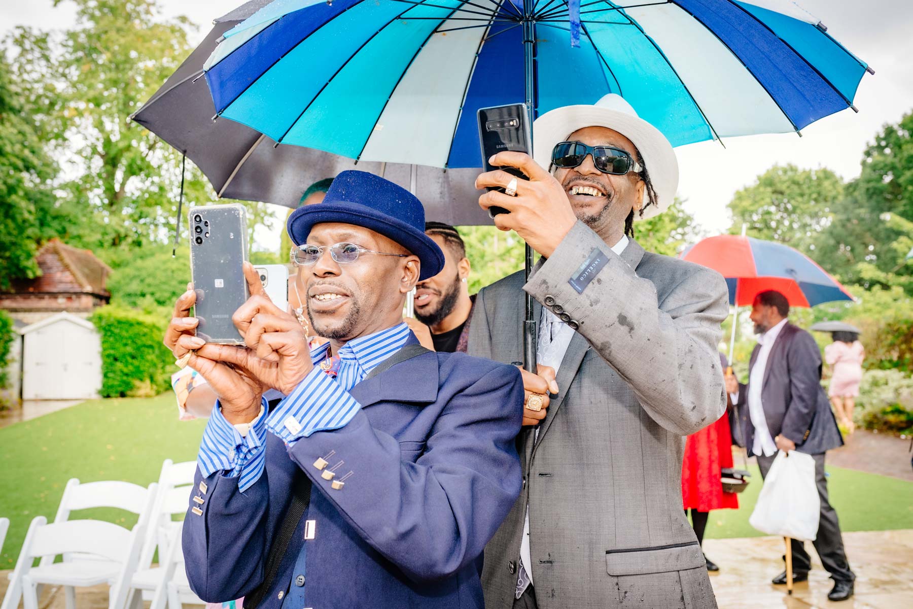 Two men holding up camera phones and smiling in the rain