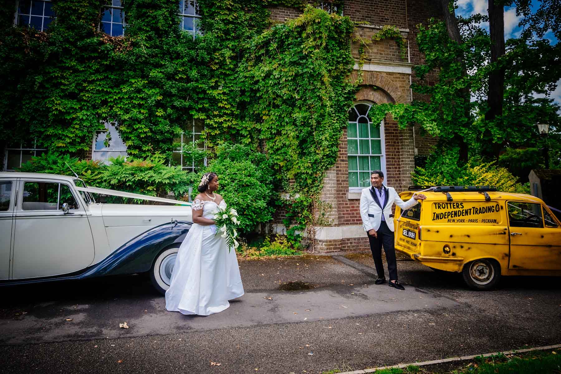 Bride and groom posing with a Rolls Royce and Del Boy's car