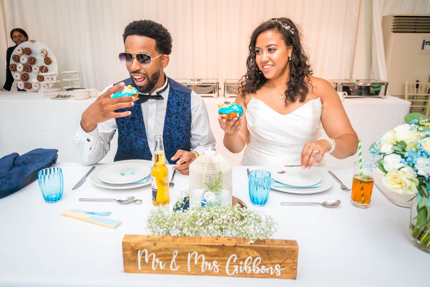 Newlyweds sitting at top table at their reception, about to eat cupcakes